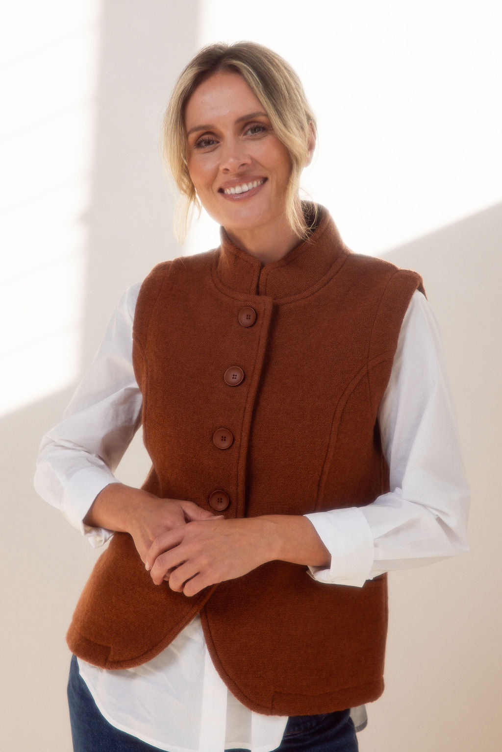 Woman wearing a copper vest over a white shirt with a plain background