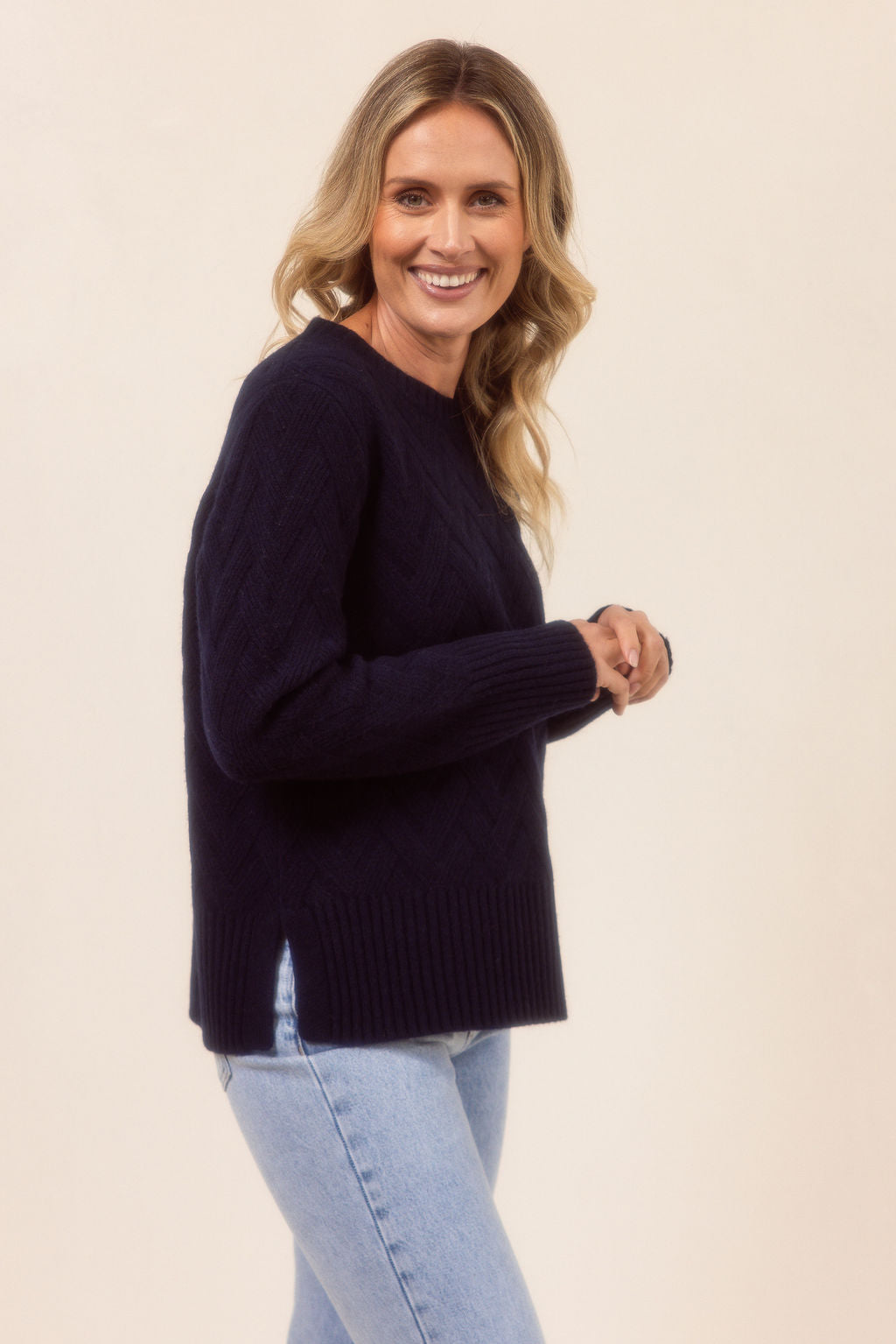 Woman wearing a navy See Saw sweater and light blue jeans on a beige background