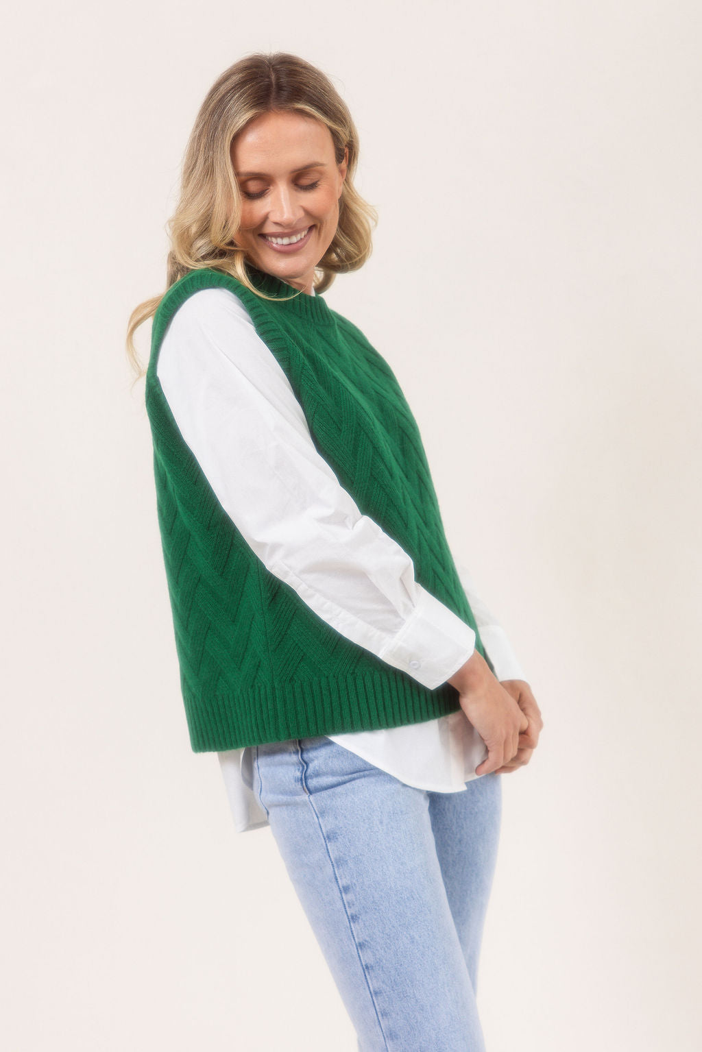 Woman wearing a See Saw green Merino Wool knitted vest over a white shirt on a plain background