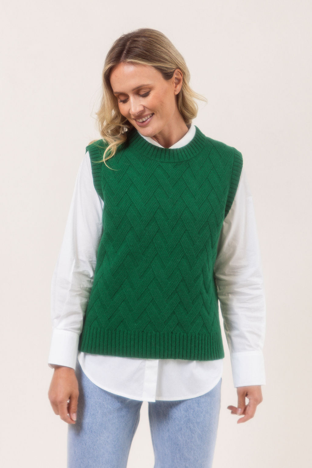 Woman wearing a See Saw green Merino Wool knitted vest over a white shirt on a plain background