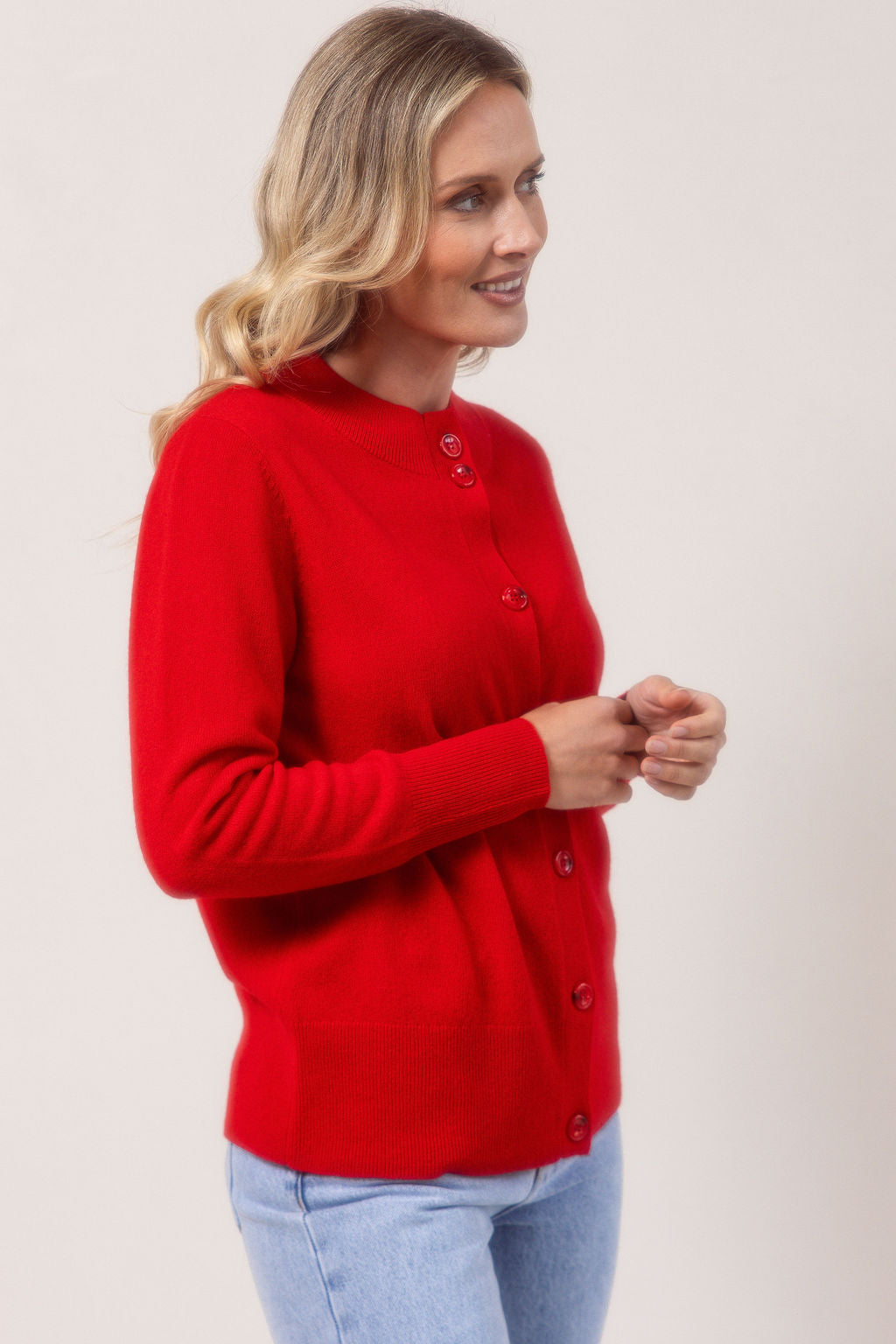 Woman wearing a merino Wool See Saw red cardigan and light blue jeans against a plain background