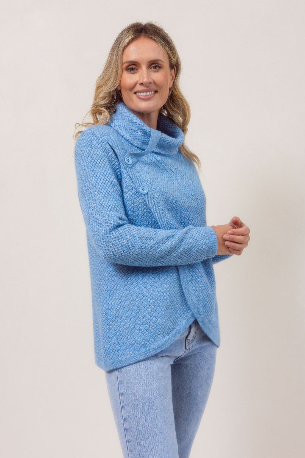 Woman wearing a powder blue Cowl Neck Moss Stitch See Saw sweater with a white background