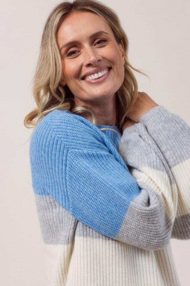 Woman wearing a blue, gray, and white striped See Saw sweater against a plain background