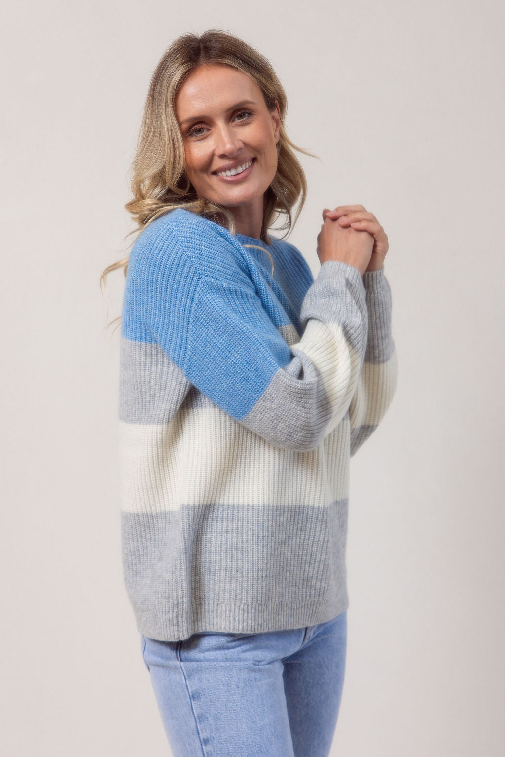 Woman wearing a blue, gray, and white striped See Saw sweater against a plain background