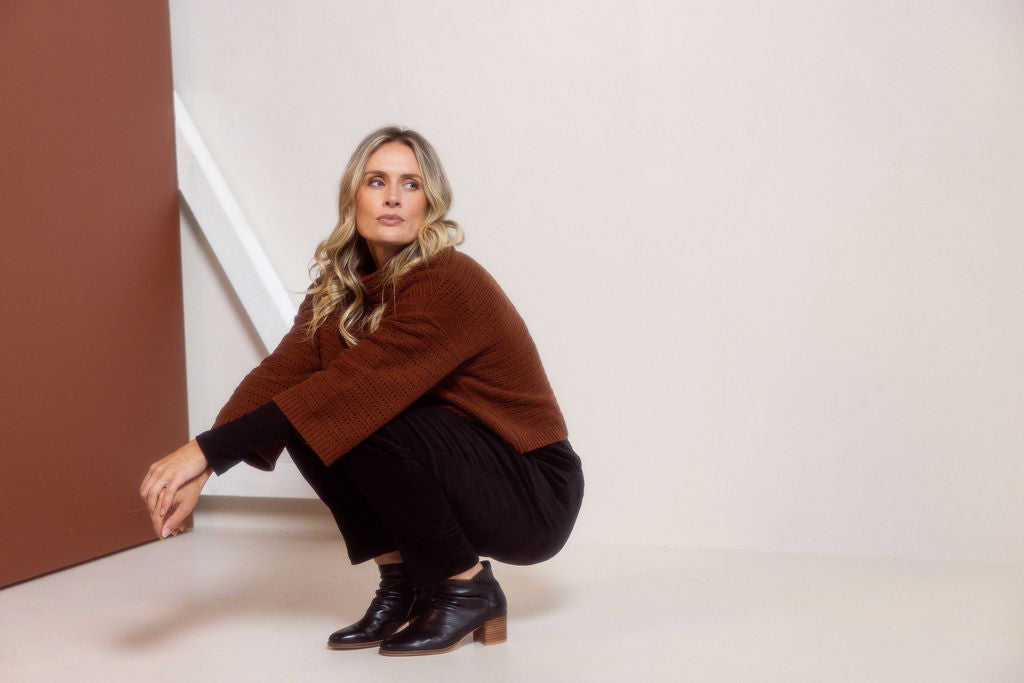 Woman wearing a See Saw copper pointelle sweater and polka dot shirt standing against a white background.