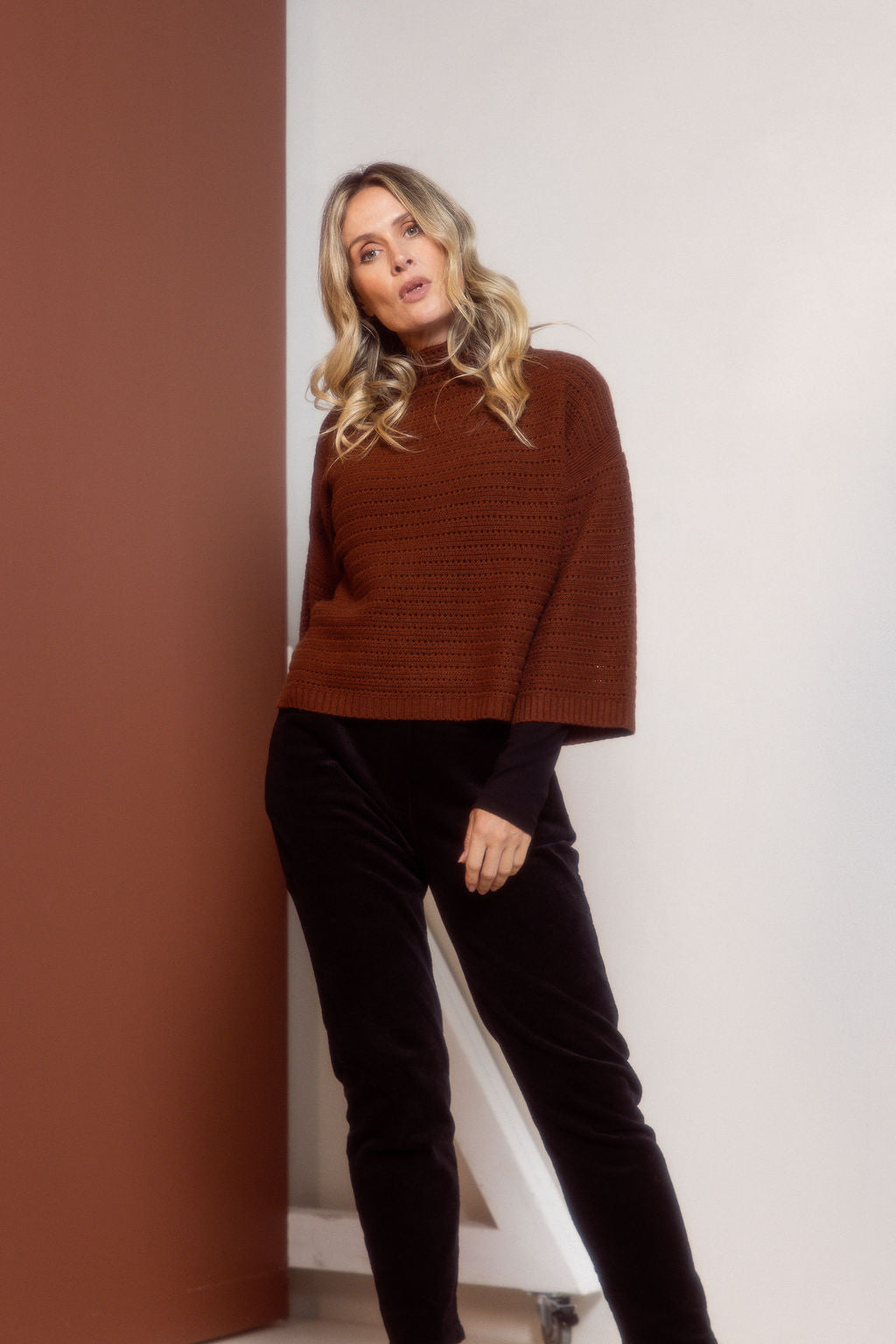 Woman wearing a See Saw copper pointelle sweater and polka dot shirt standing against a white background.