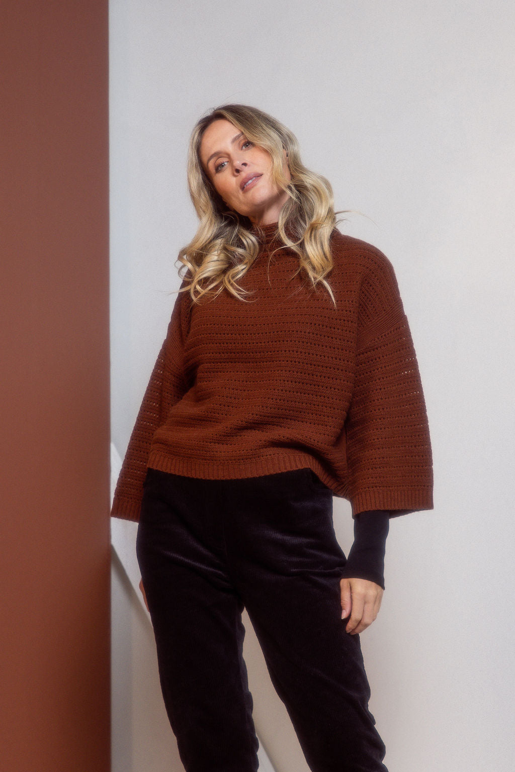 Woman wearing a See Saw copper pointelle sweater and polka dot shirt standing against a white background.