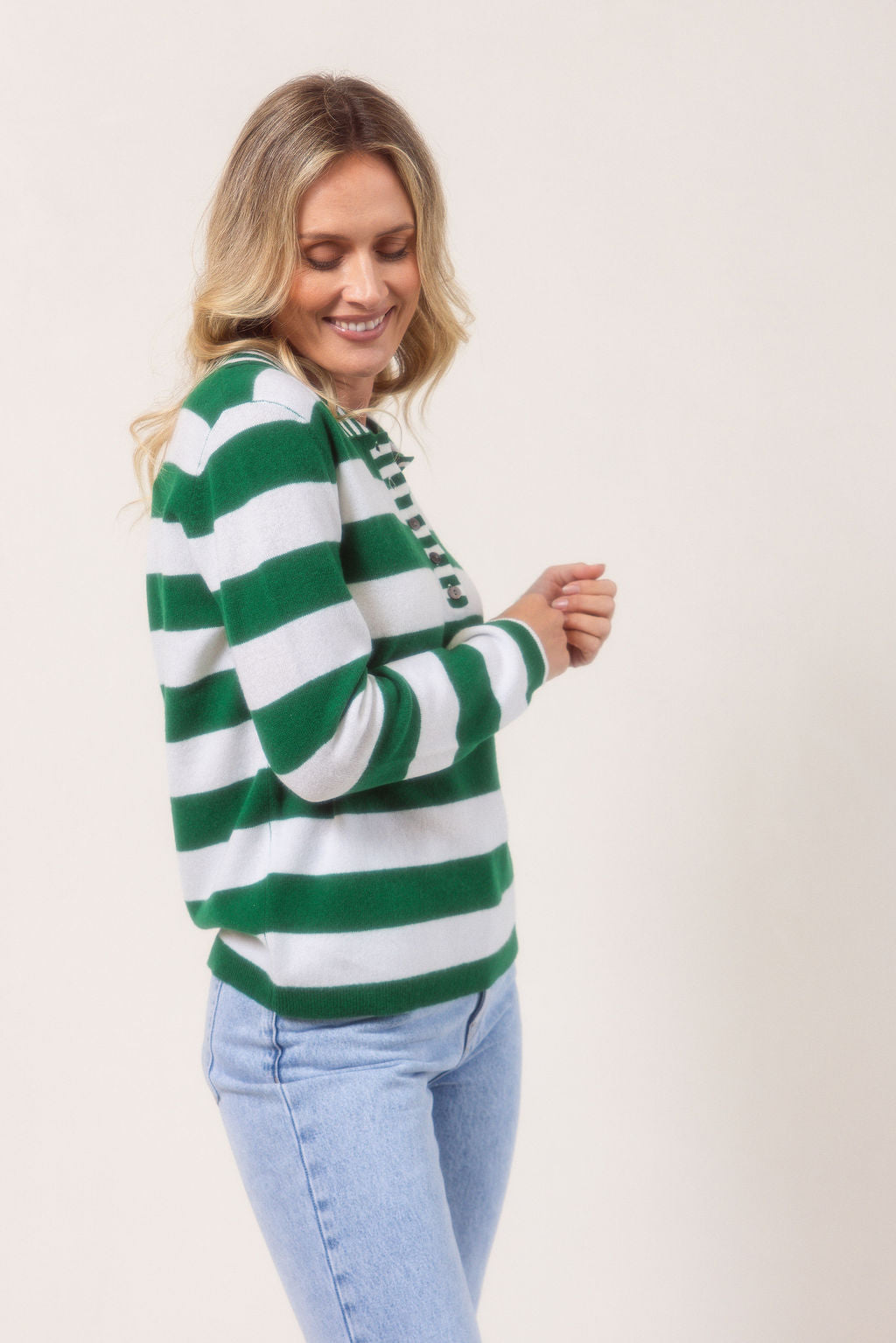Woman wearing a merino wool See Saw green and white striped sweater on a plain background