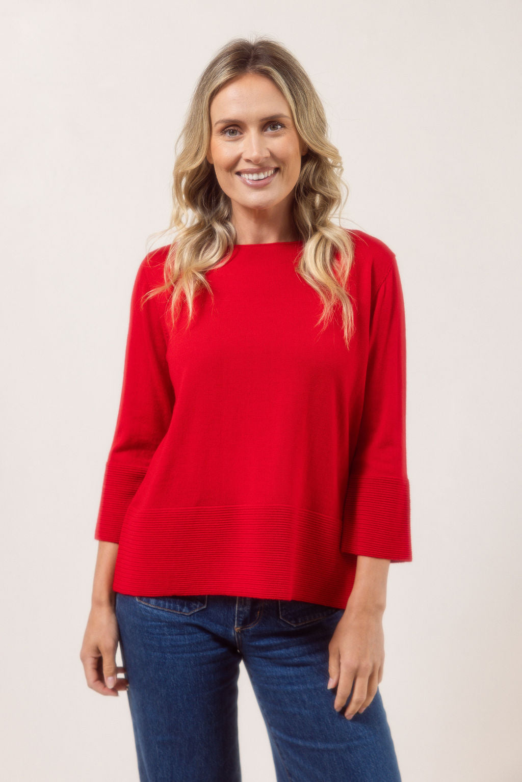 Woman wearing a red See Saw Merino Wool sweater and patterned scarf against a white background