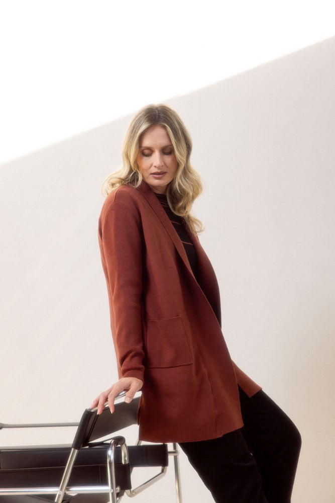 Woman wearing a brown See Saw cardigan standing next to a chair against a white background