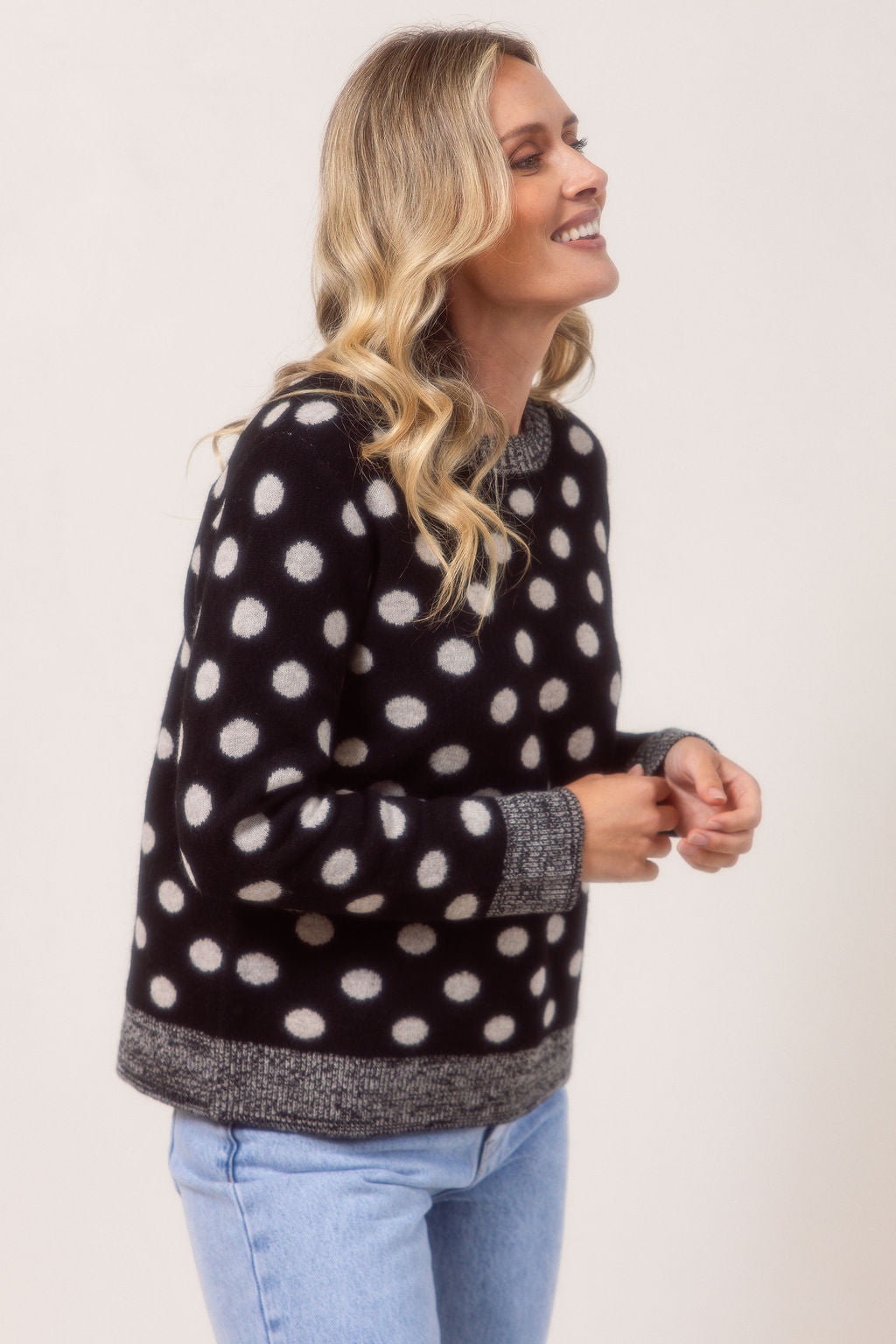 Woman wearing a See Saw Merino Wool sweater with polka dots and light blue jeans on a plain background.