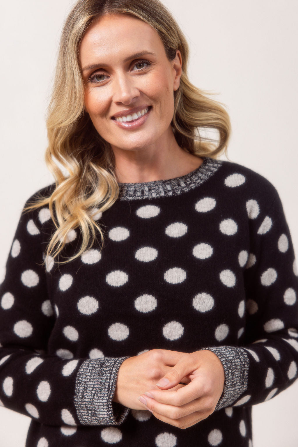 Woman wearing a See Saw Merino Wool sweater with polka dots and light blue jeans on a plain background.
