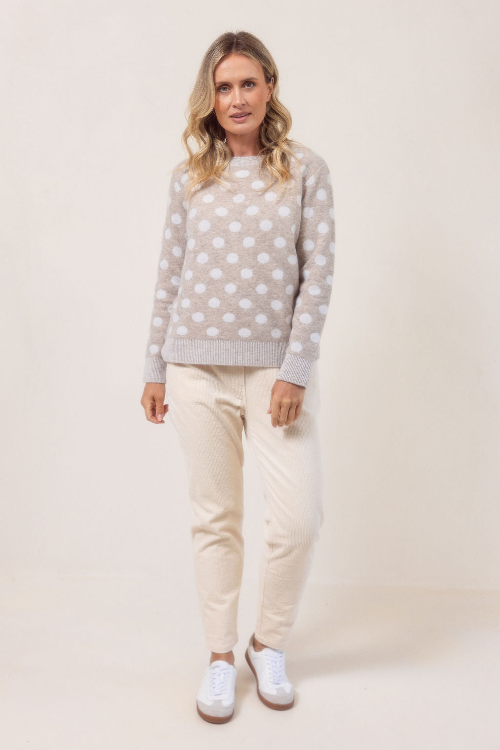 Woman wearing a See Saw Merino Wool sweater with polka dots and corduroy joggers on a plain background.