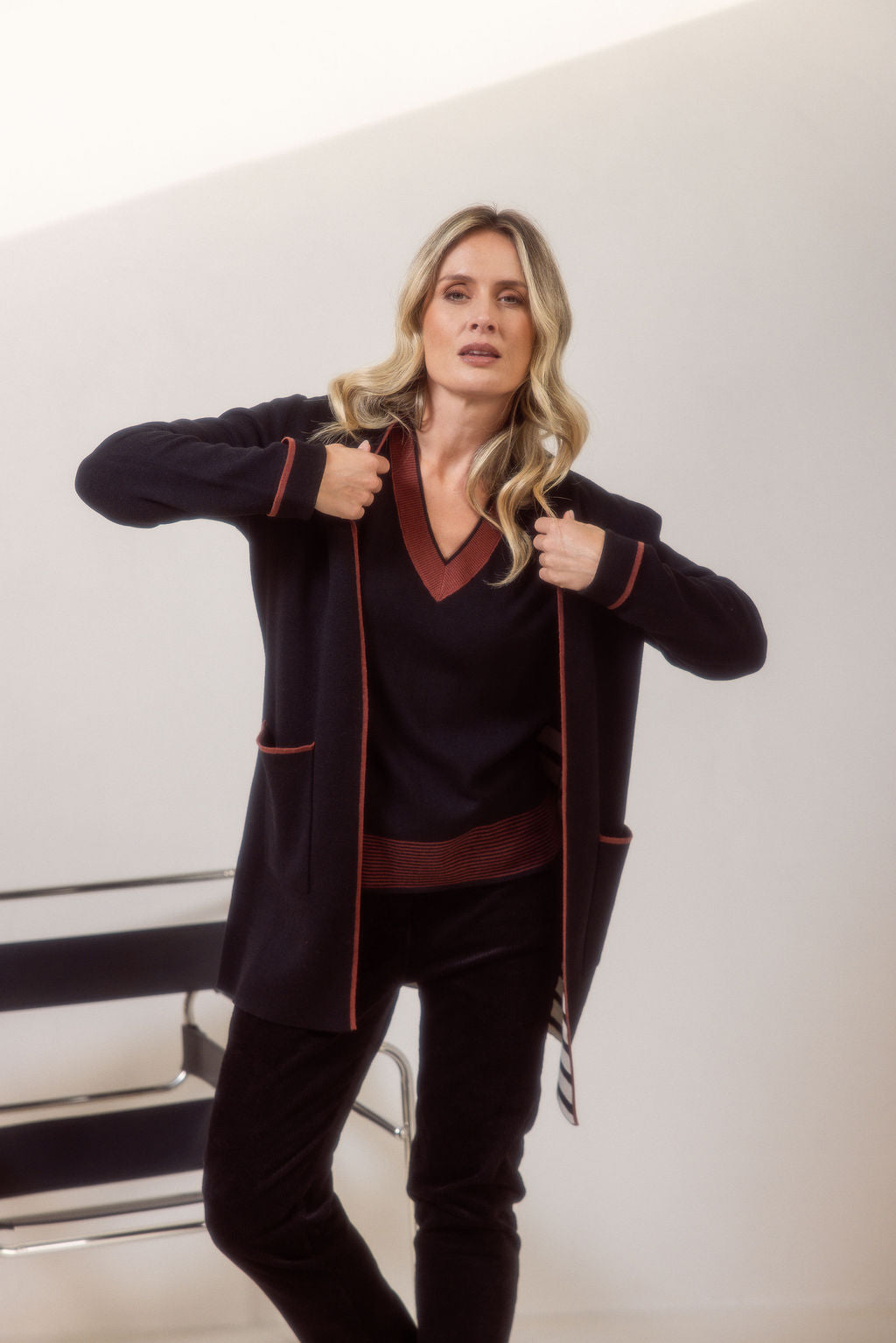 Woman wearing a See Saw black cardigan with copper trim, black sweater and pants and black boots on a plain background