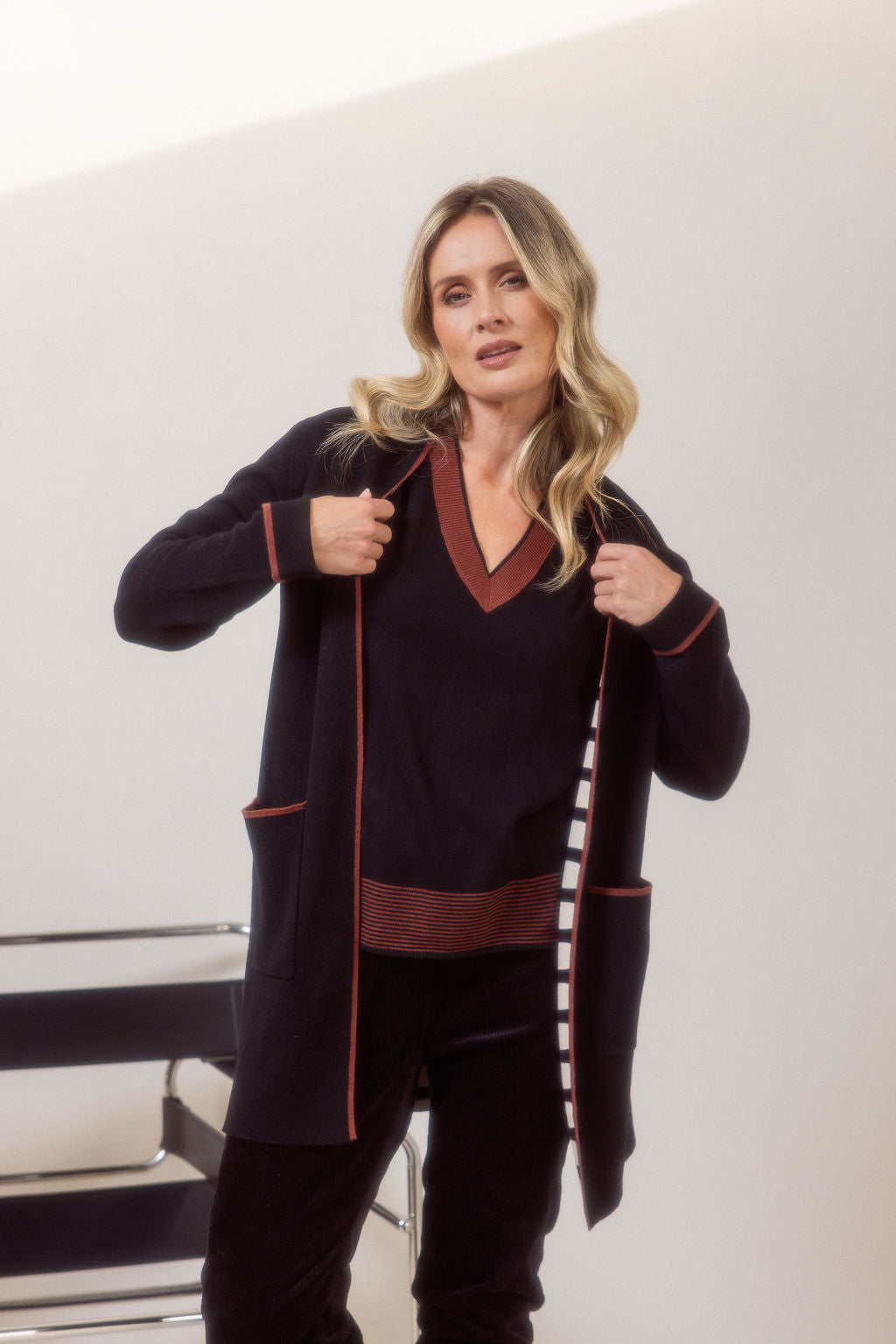 Woman wearing a See Saw black cardigan with copper trim, black sweater and pants and black boots on a plain background