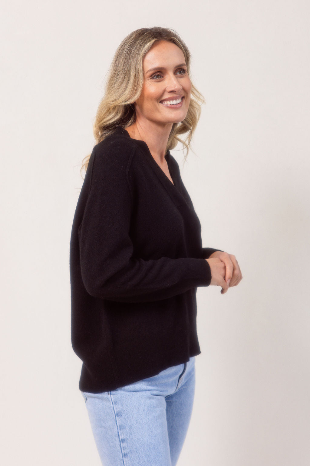 Woman wearing a v neck Merino wool See Saw Navy sweater against a plain background