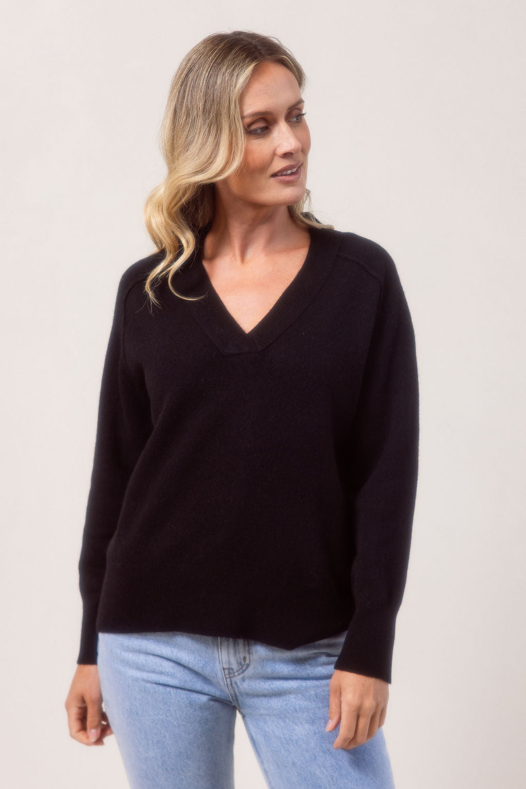 Woman wearing a v neck Merino wool See Saw Navy sweater against a plain background