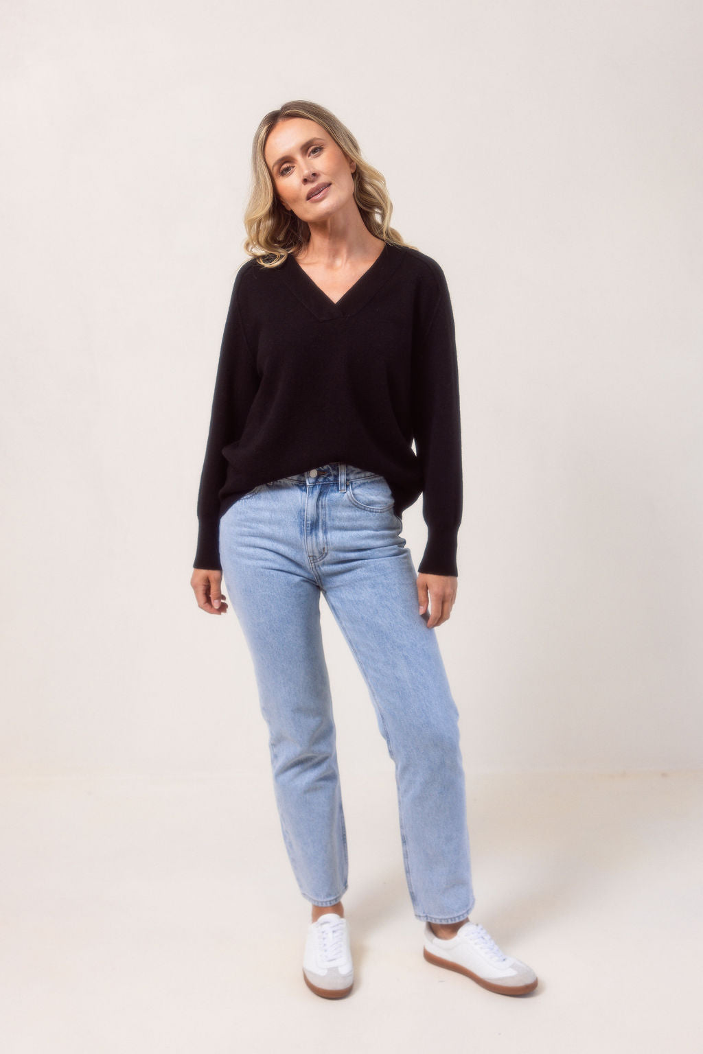 Woman wearing a v neck Merino wool See Saw Navy sweater against a plain background