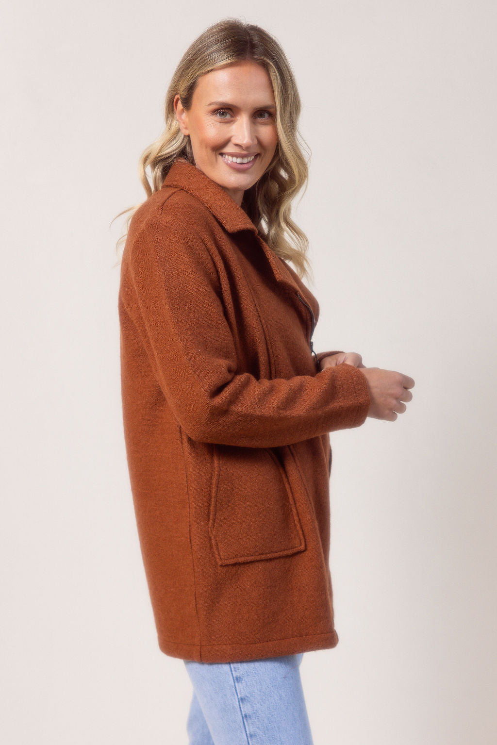 Woman wearing a copper See Saw boiled wool coat against a plain background