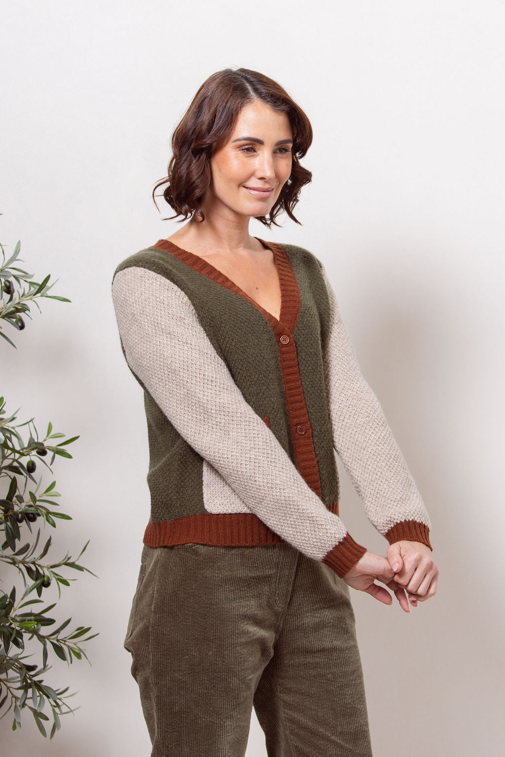 Woman wearing a Moss Stitch See Saw green and beige cardigan with brown accents on a white background