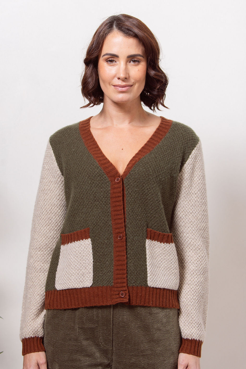 Woman wearing a Moss Stitch See Saw green and beige cardigan with brown accents on a white background