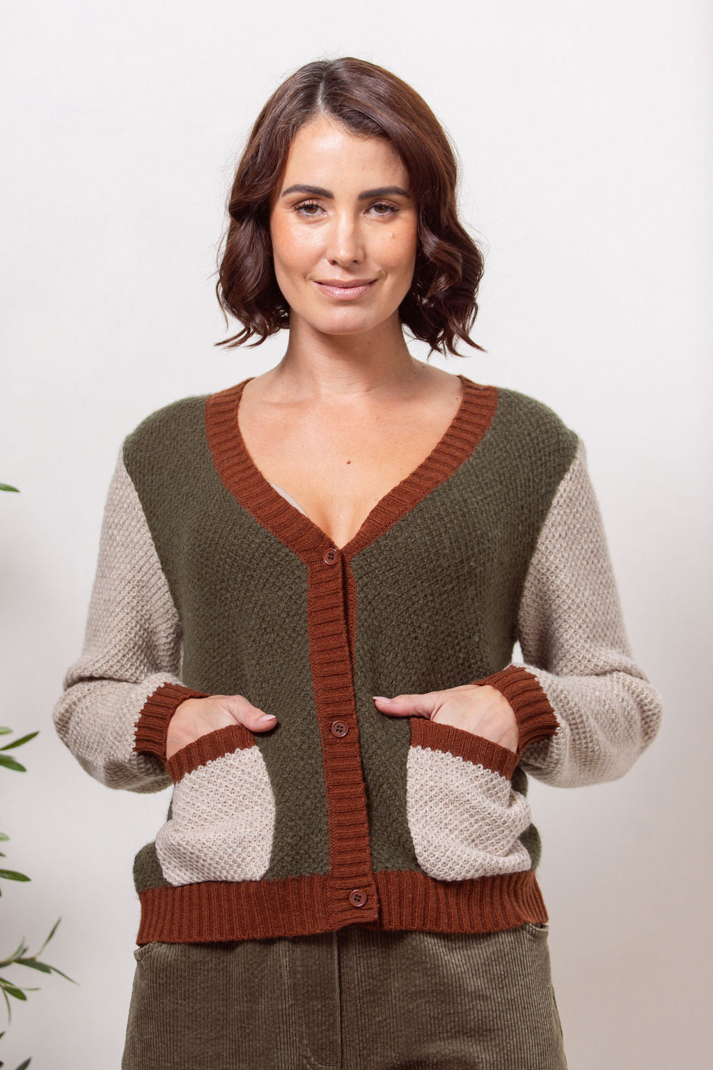 Woman wearing a Moss Stitch See Saw green and beige cardigan with brown accents on a white background