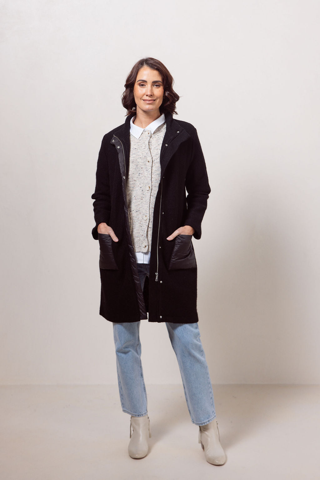 Woman wearing a black boiled wool See Saw coat over a patterned sweater on a plain background