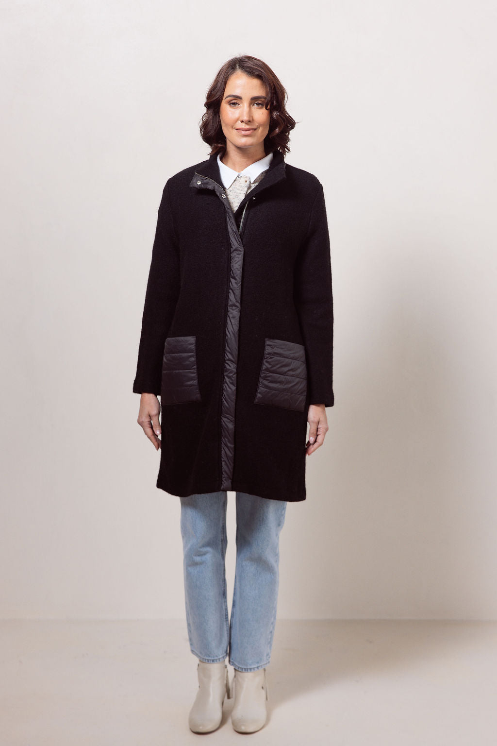 Woman wearing a black boiled wool See Saw coat over a patterned sweater on a plain background