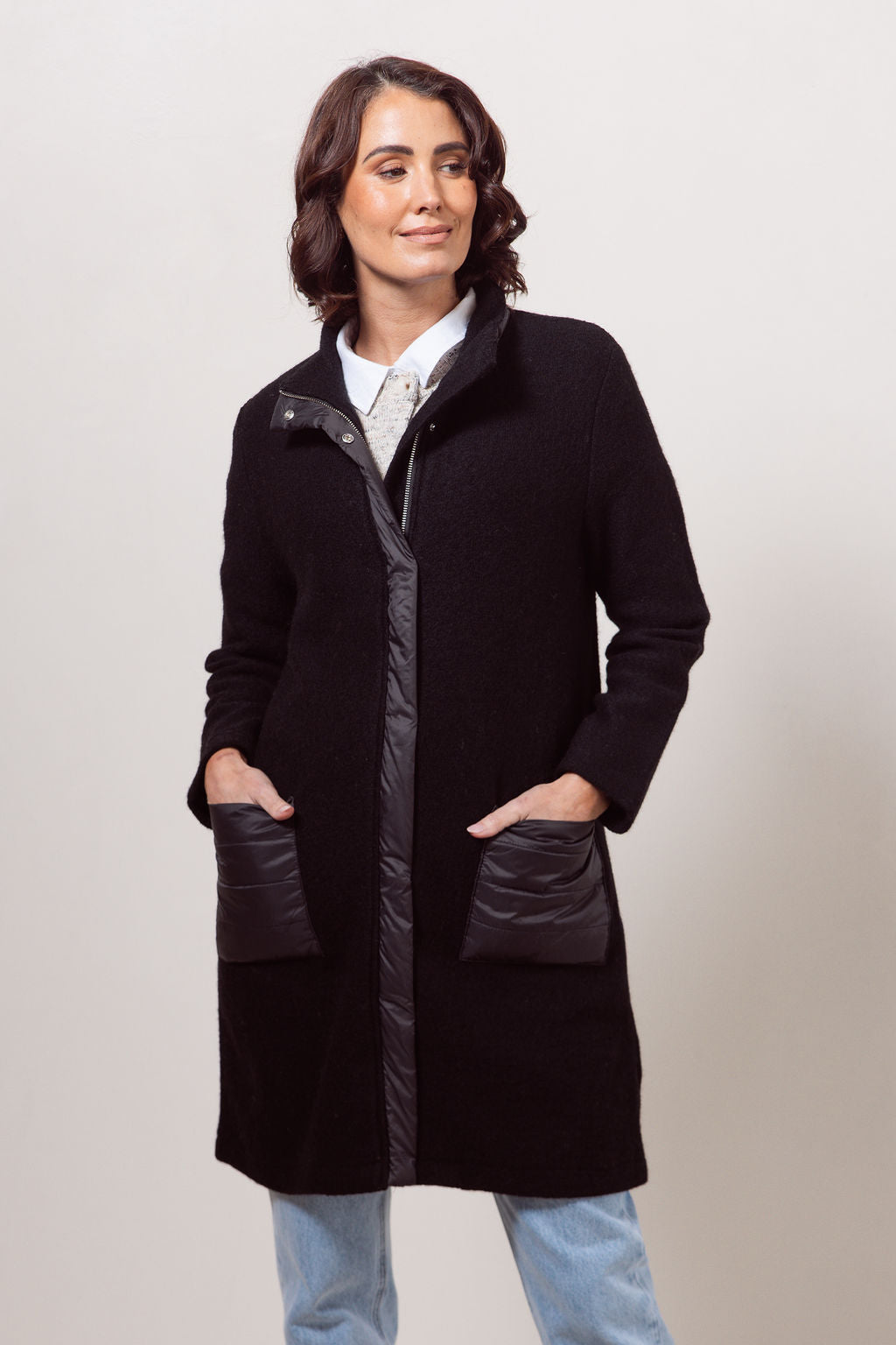 Woman wearing a black boiled wool See Saw coat over a patterned sweater on a plain background