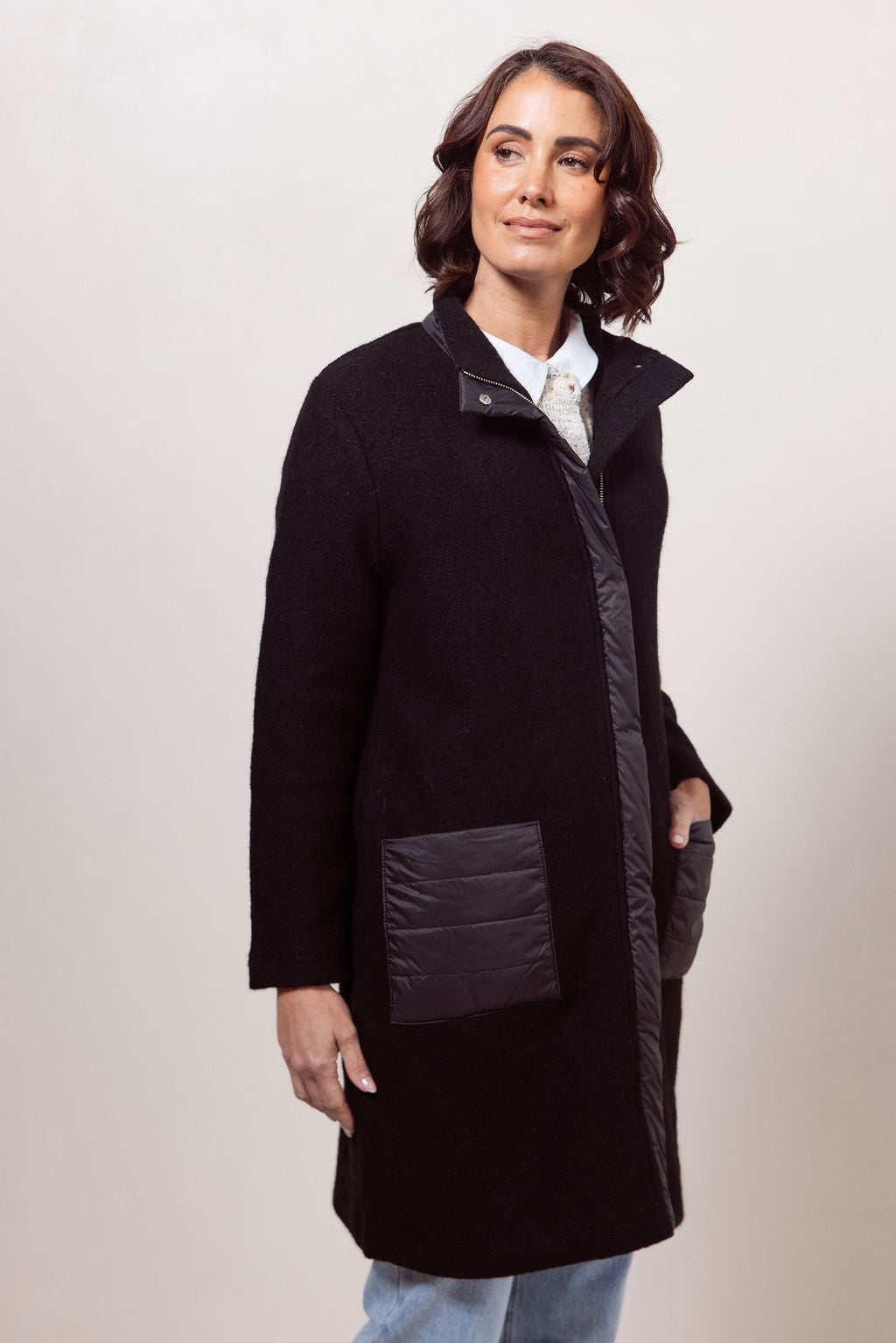 Woman wearing a navy boiled wool See Saw coat over a patterned sweater on a plain background