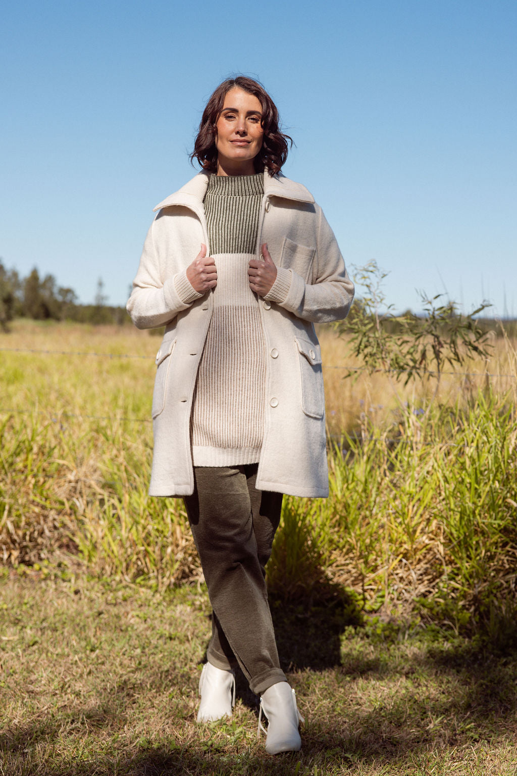 Woman standing in a field wearing a long boiled wool See Saw coat, sweater, and pants.
