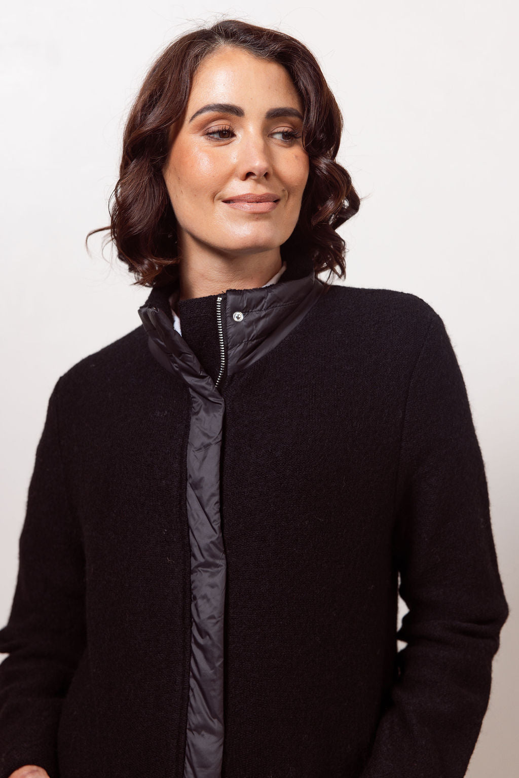 Woman wearing a black boiled wool See Saw coat over a patterned sweater on a plain background