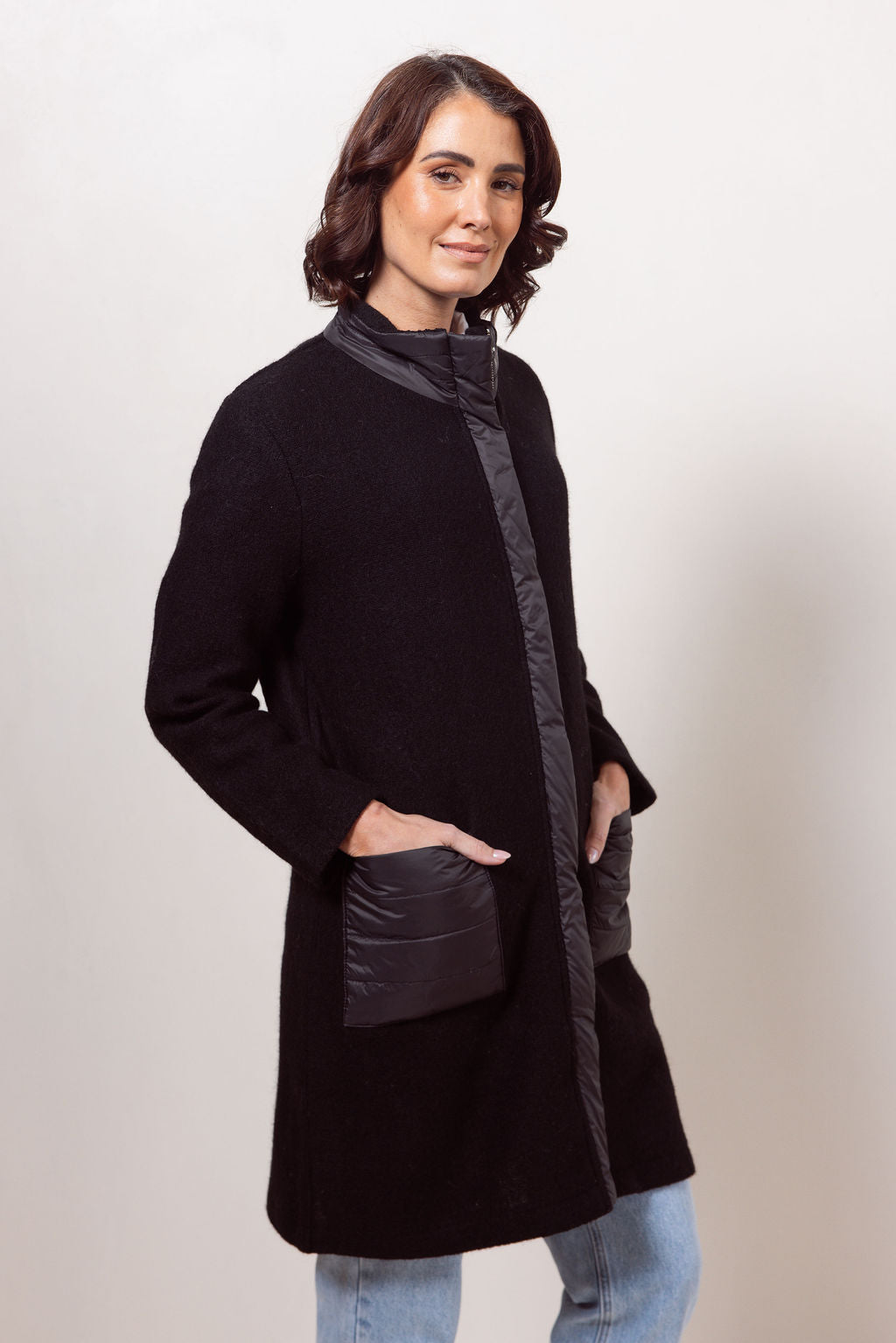 Woman wearing a black boiled wool See Saw coat over a patterned sweater on a plain background