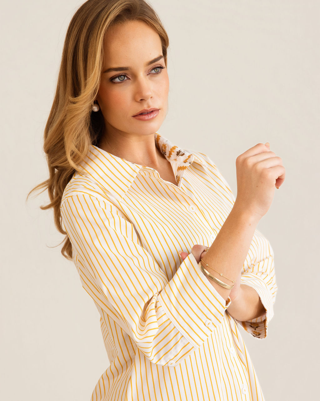 A woman modeling a yellow and white Kaleido cotton vertically striped button-down shirt dress with three-quarter sleeves, standing against a plain off-white studio background.