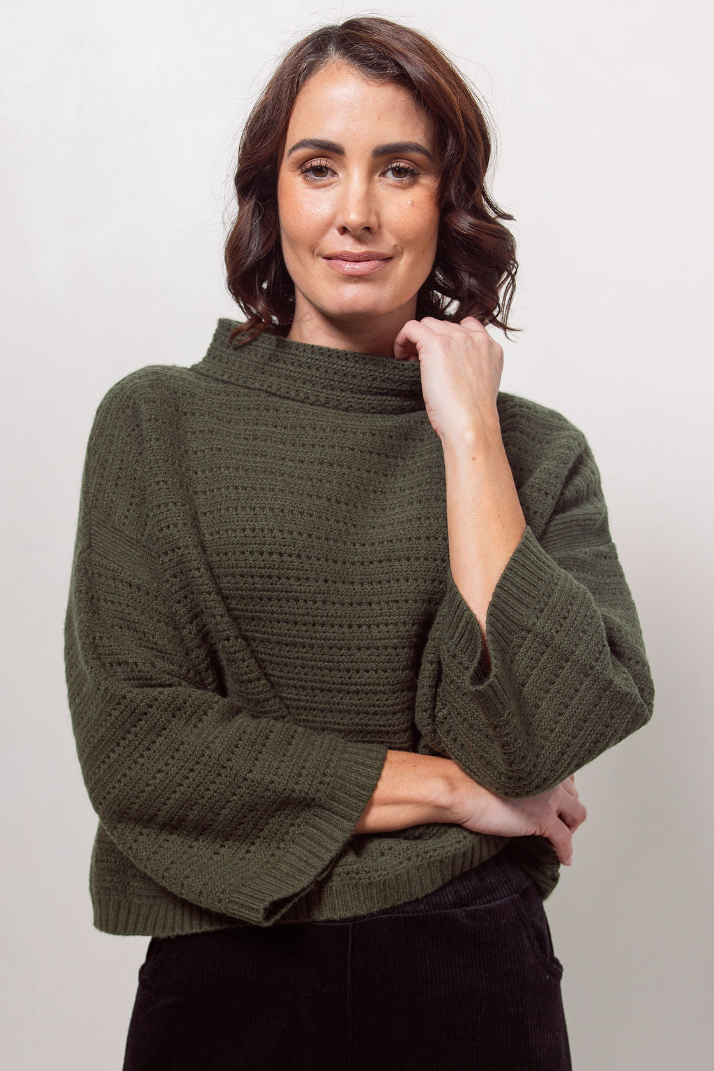 Woman wearing a See Saw Khaki pointelle sweater and polka dot shirt standing against a white background.