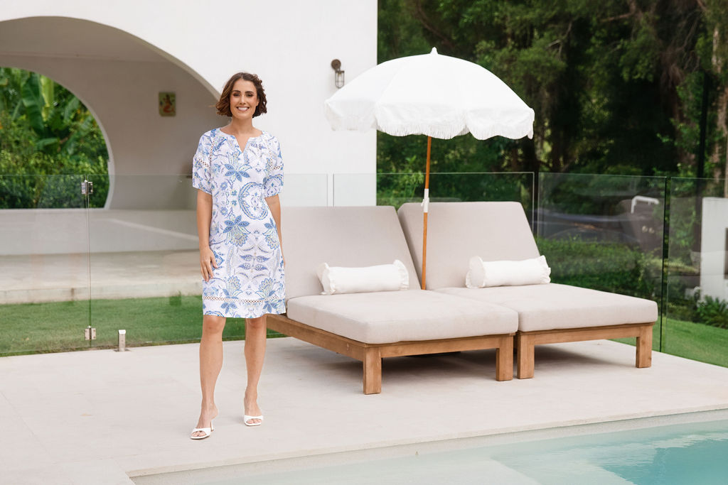 Woman modelling see saw linen dress in botanica print with lace trim in a n outdoor pool area.