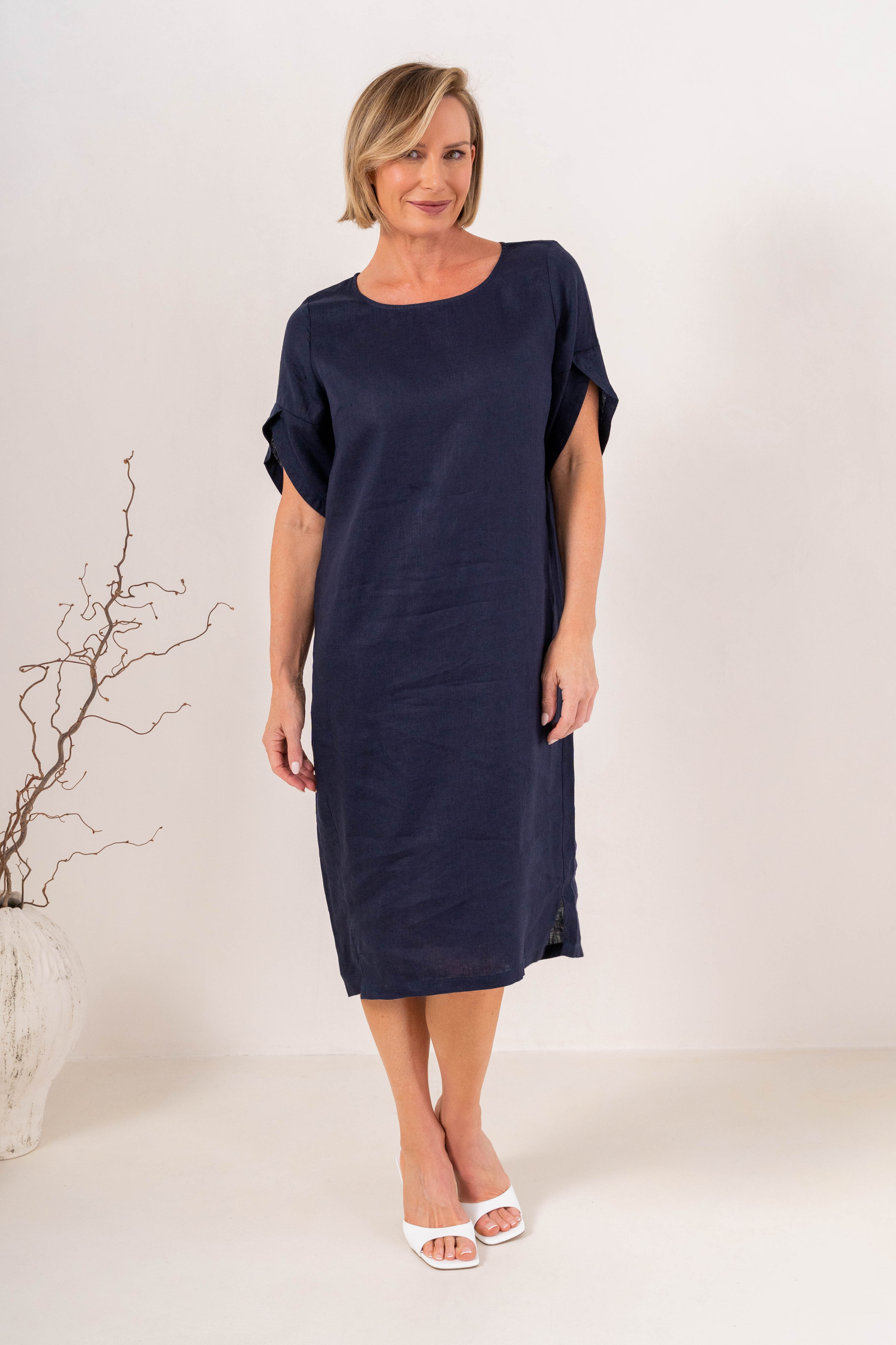 A woman modeling a See Saw Linen navy short-sleeve midi dress with a relaxed fit, standing against a plain off-white studio background.