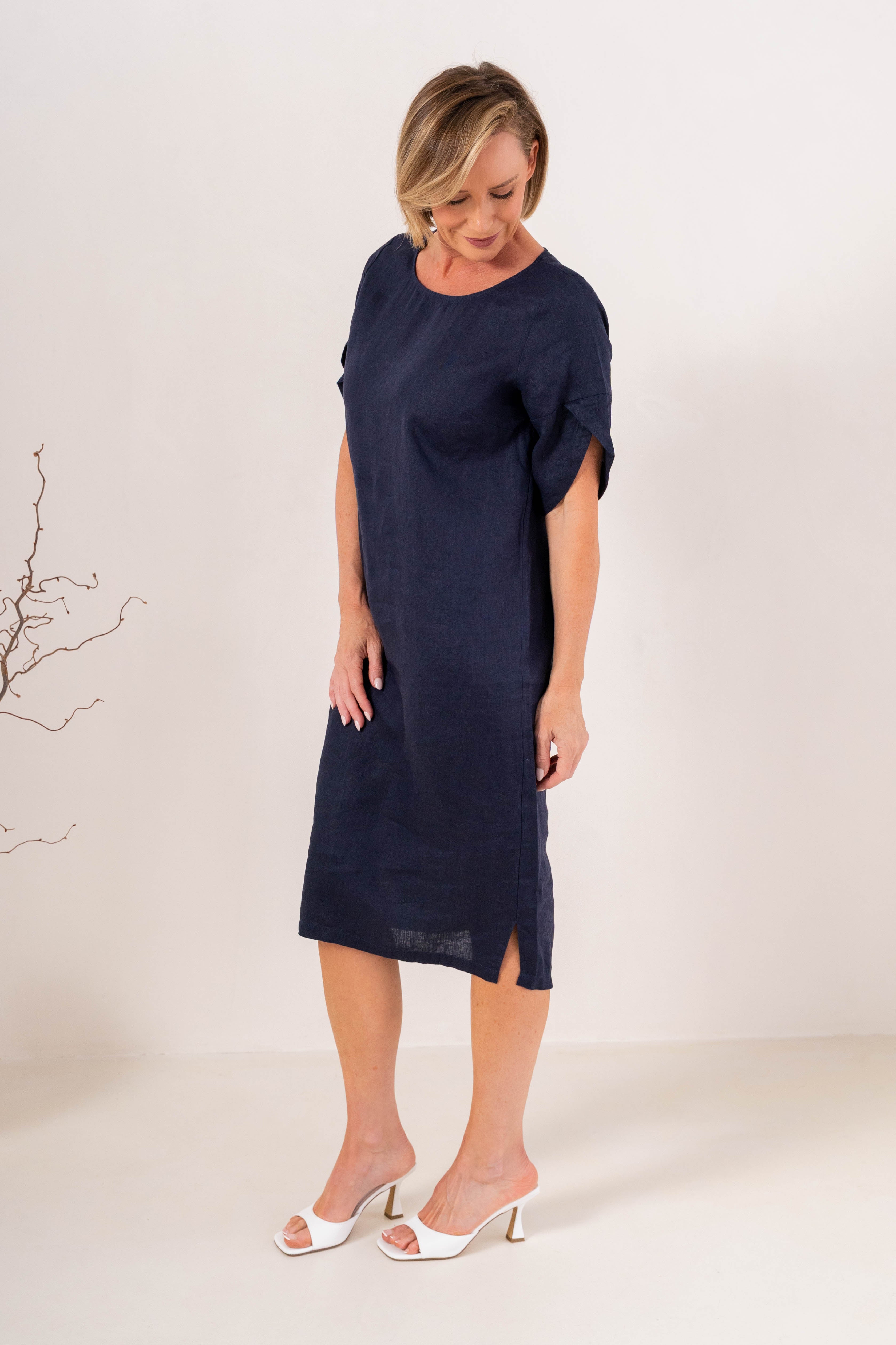 A woman modeling a See Saw Linen navy blue short-sleeve midi dress with a relaxed fit, standing against a plain off-white studio background.