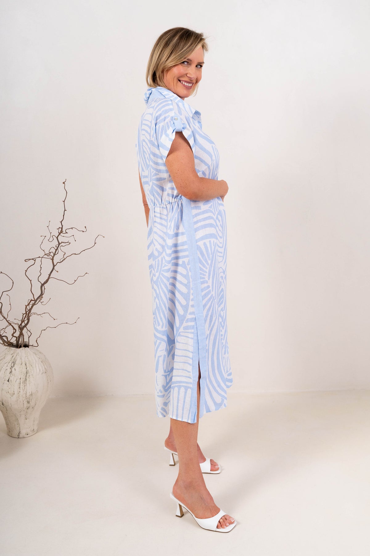 A woman modeling a Palm Breeze Linen See Saw abstract patterned midi shirt dress with short sleeves, a button-down collar, and a front slit, standing in a studio setting.