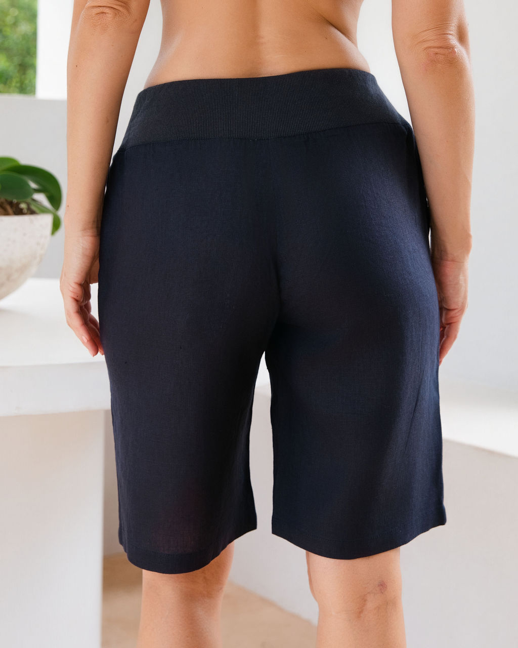 Navy linen See Saw linen shorts with a contrasting light blue elastic waistband, shown on a model from the waist down in a bright indoor setting.