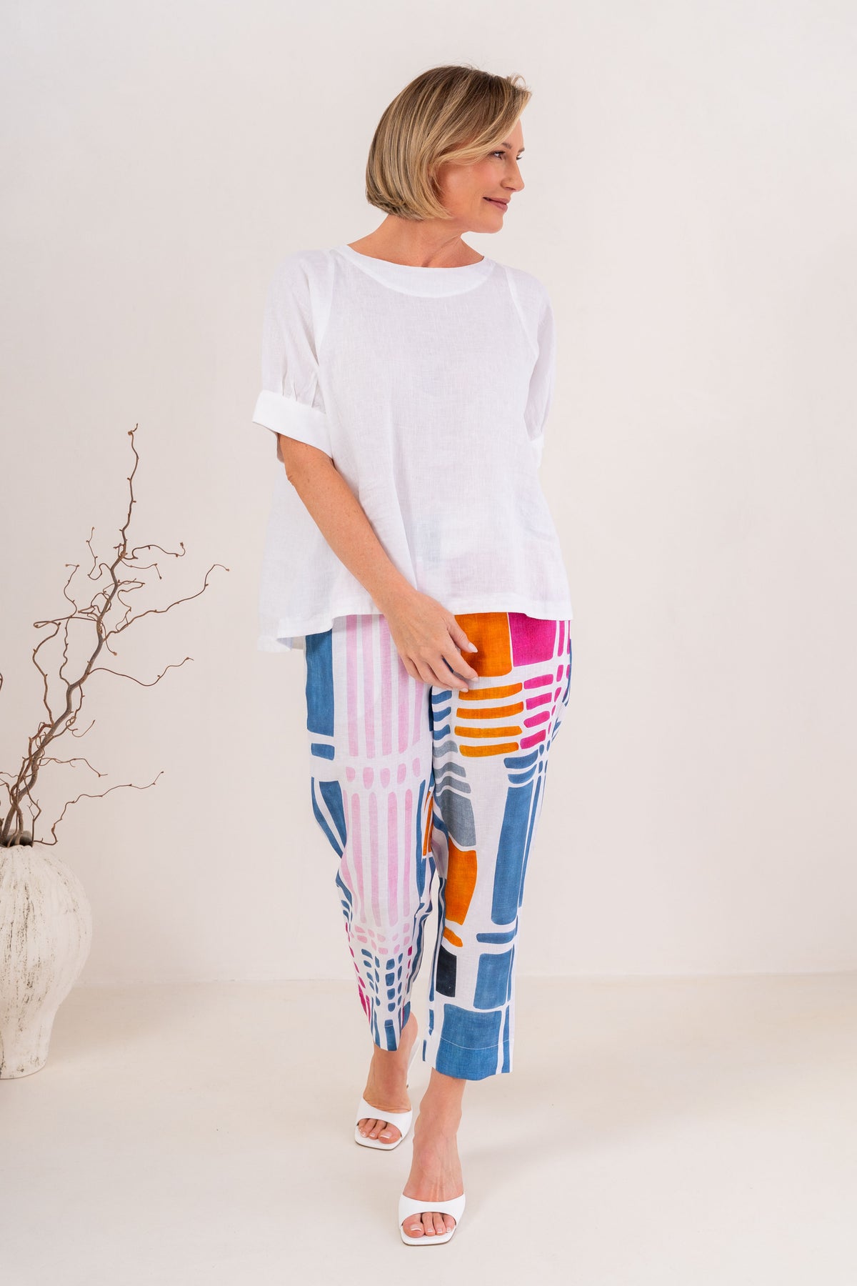 Woman modelling 100% linen See Saw pant in gallery print and in a 7/8 length. Modelling against a neutral studio background.