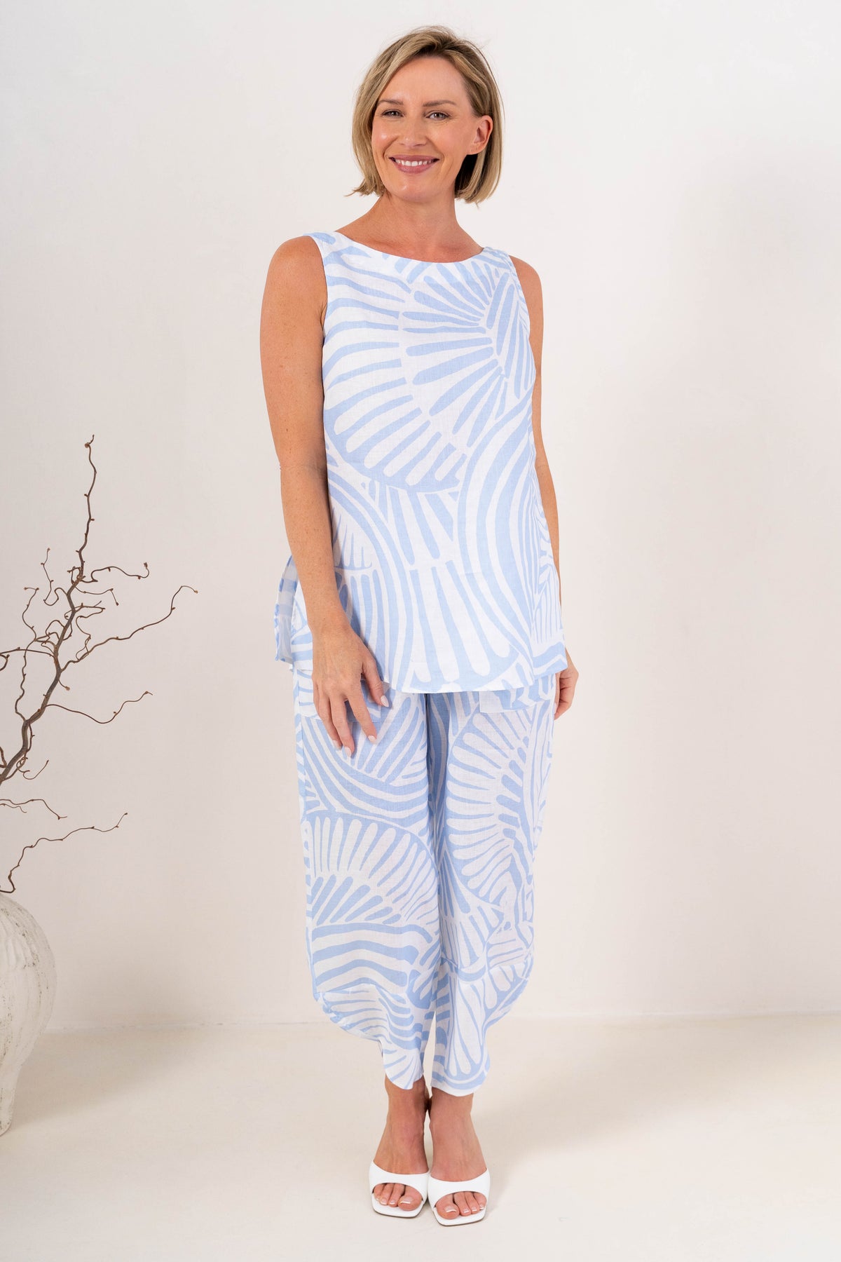 A woman modeling a light blue Palm breeze linen See Saw sleeveless tunic top and matching wide-leg pants set, standing against a plain off-white studio background.