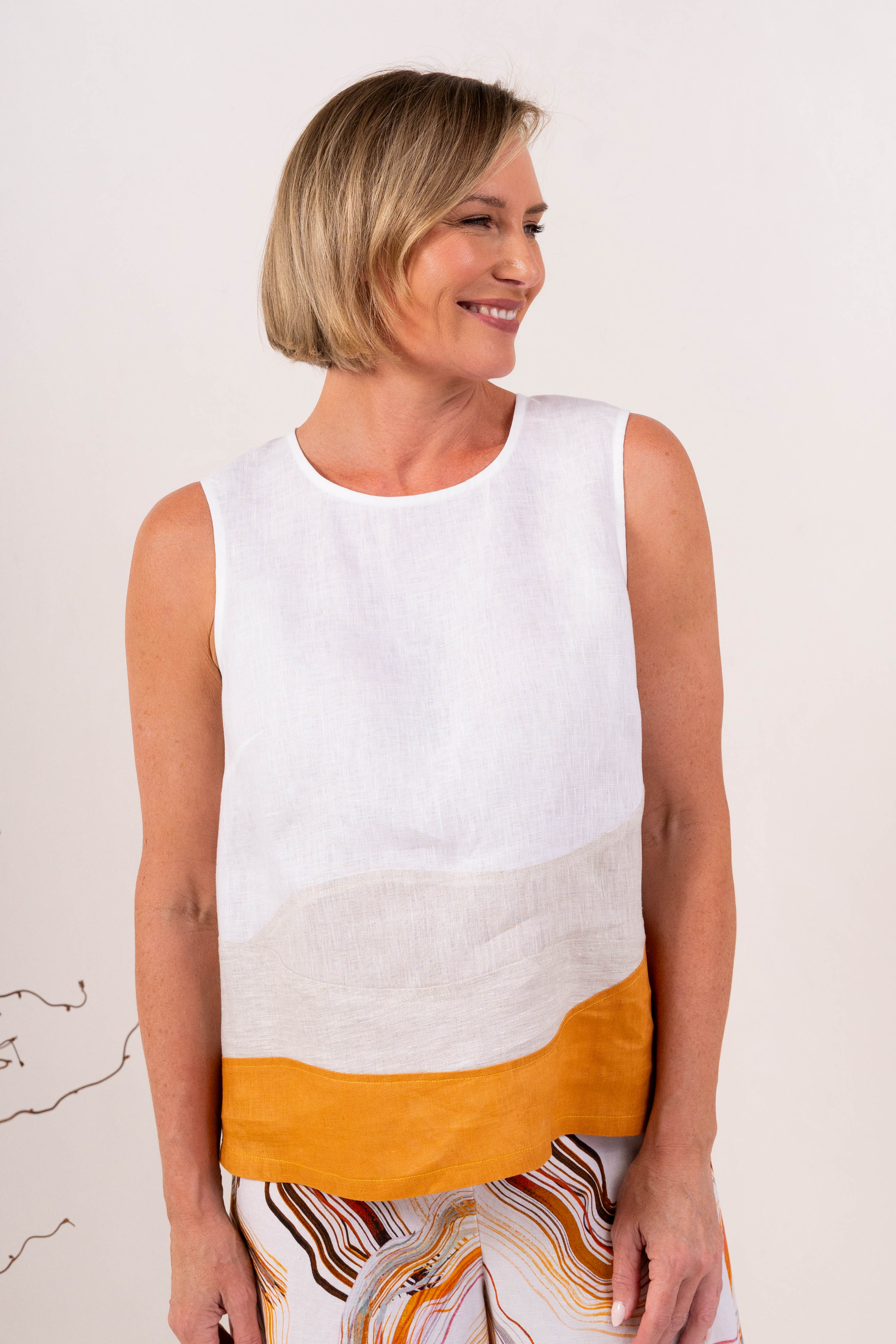 A woman modeling a sleeveless See Saw Linen color-block top and matching wide-leg trousers in navy, off-white, and light beige, standing against a plain light background.