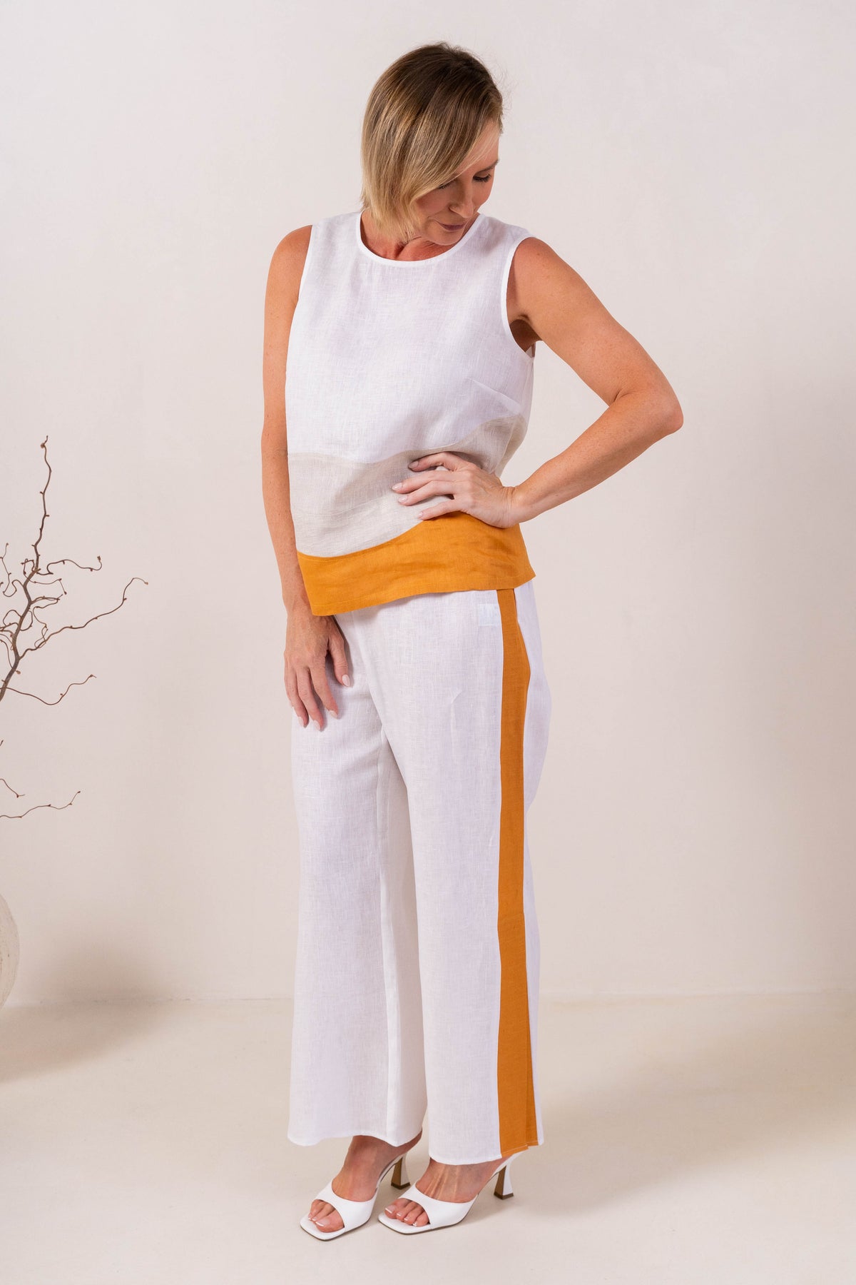 A woman modeling a sleeveless See Saw Linen color-block top and matching wide-leg trousers in navy, off-white, and light beige, standing against a plain light background.