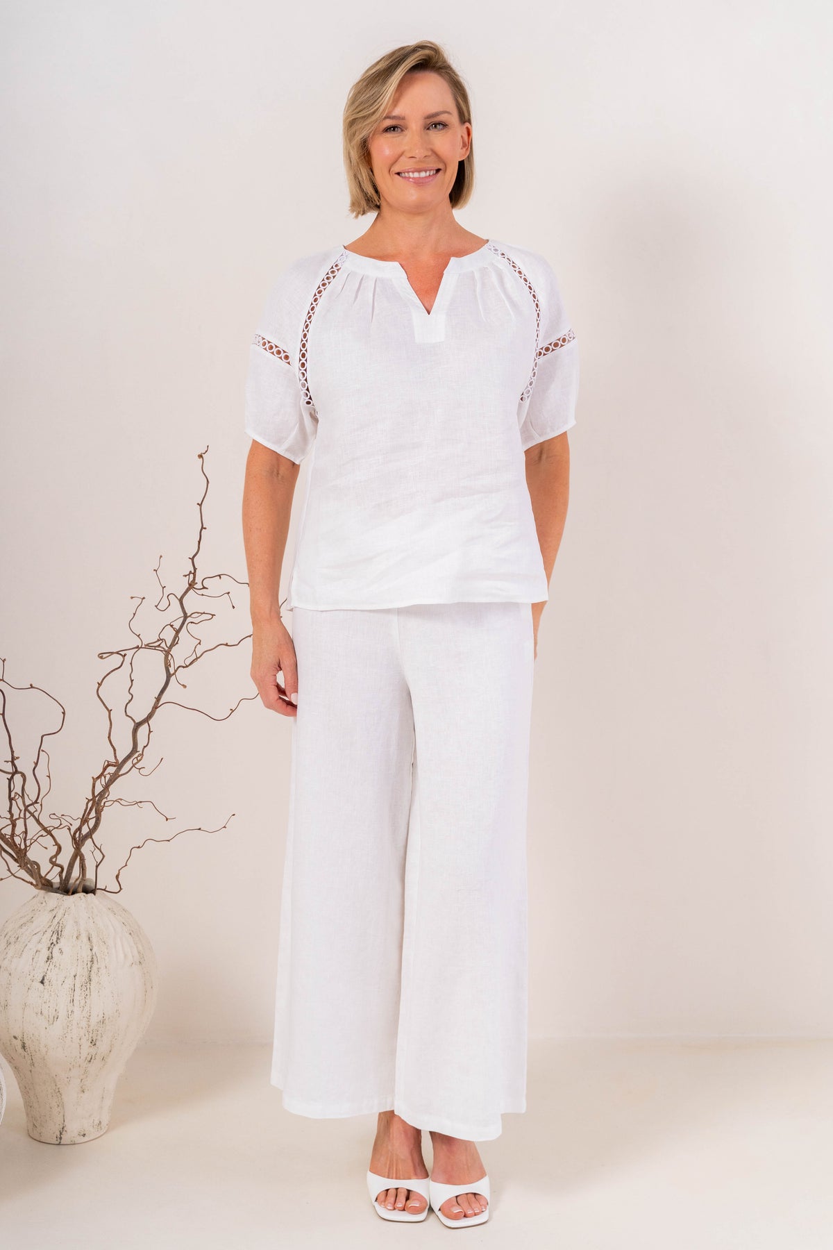 White wide-leg See Saw Palazzo linen pants shown on a model wearing white heeled sandals against a light beige background.