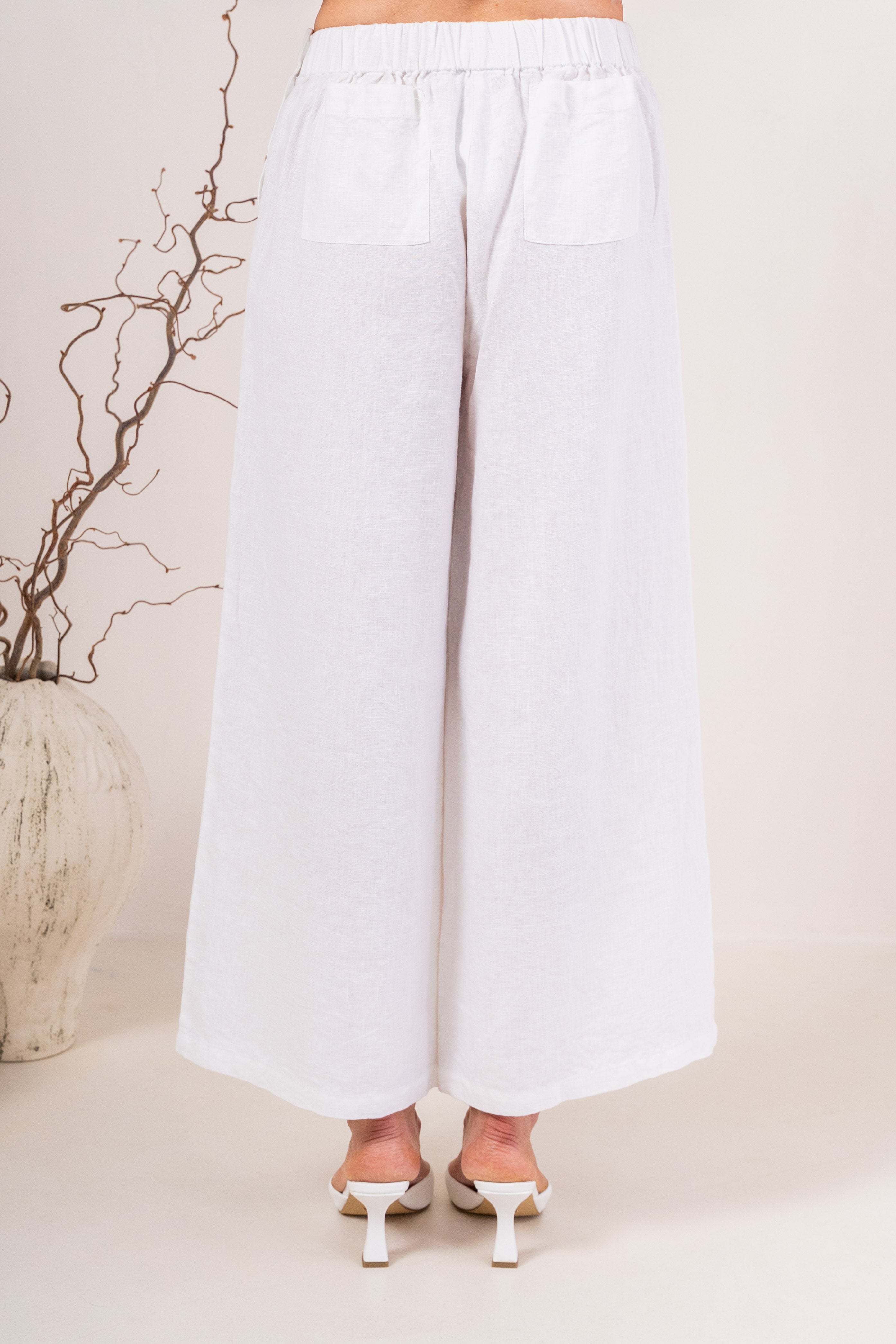 White wide-leg See Saw Palazzo linen pants shown on a model wearing white heeled sandals against a light beige background.