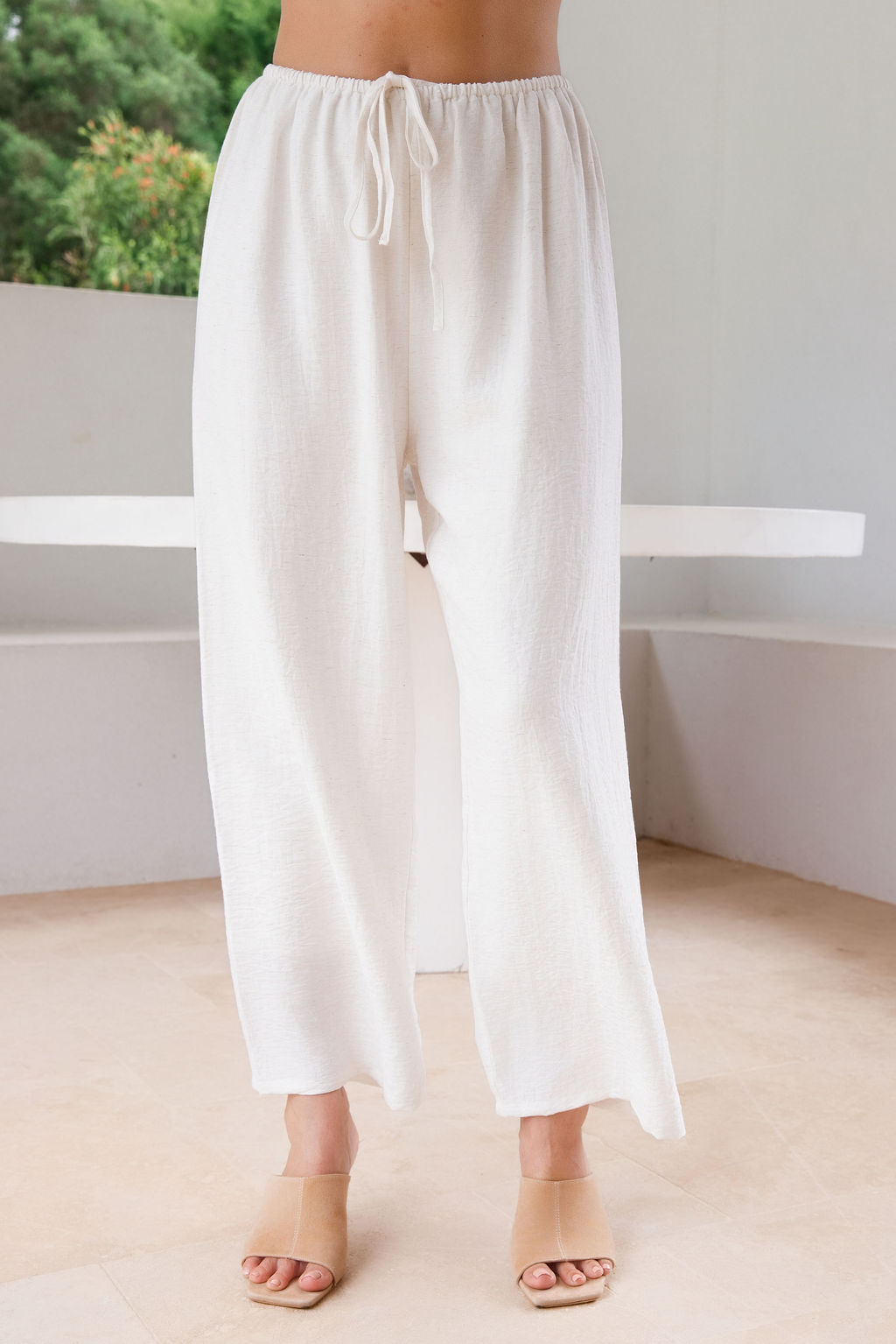 Model wearing See Saw Matching tank and pant in white in linen and rayon blend. standing in an outdoor architecturally designed patio.