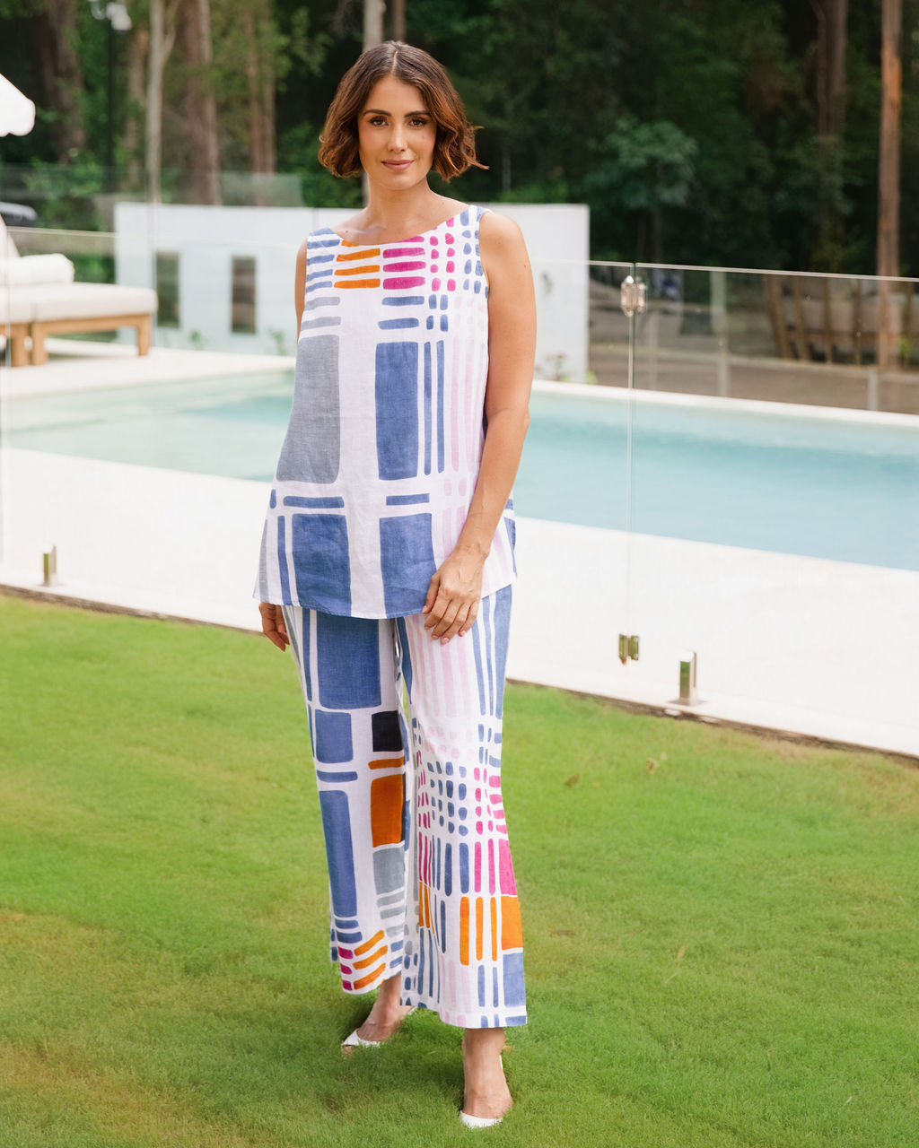 Woman modelling 100% Linen Gallery print boat neck tank by See Saw Clothing. The woman is standing outdoors in a pool area and garden setting.