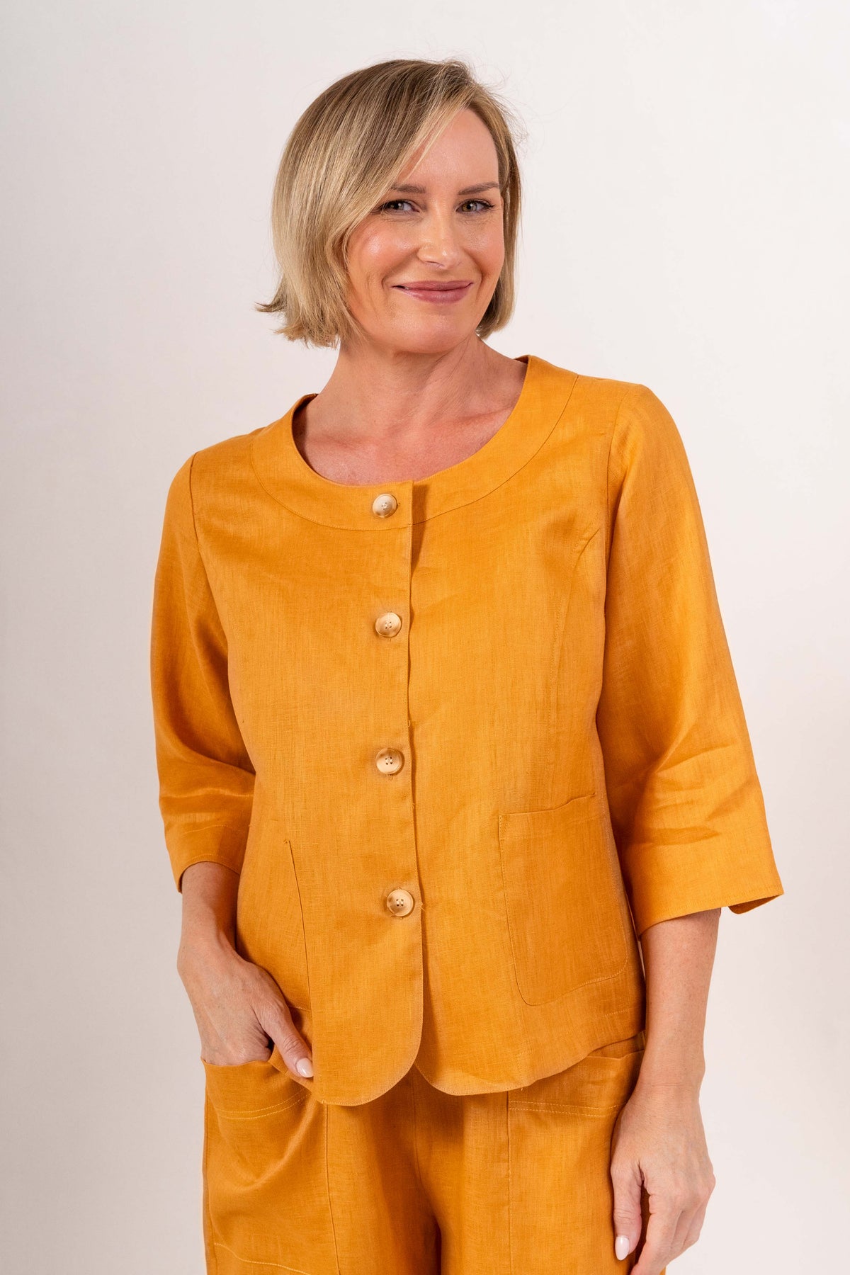 Woman modelling marigold linen see saw utility jacket top and marigold pants and against a plain background.