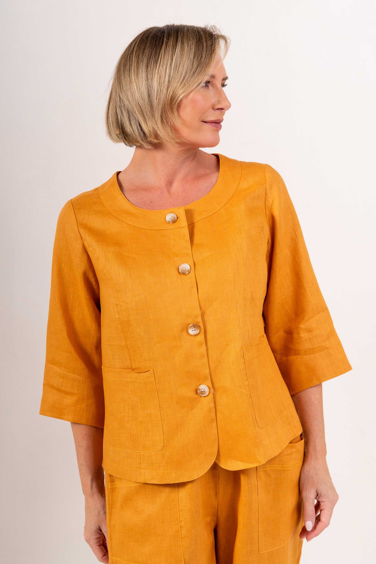 Woman modelling marigold linen see saw utility jacket top and marigold pants and against a plain background.